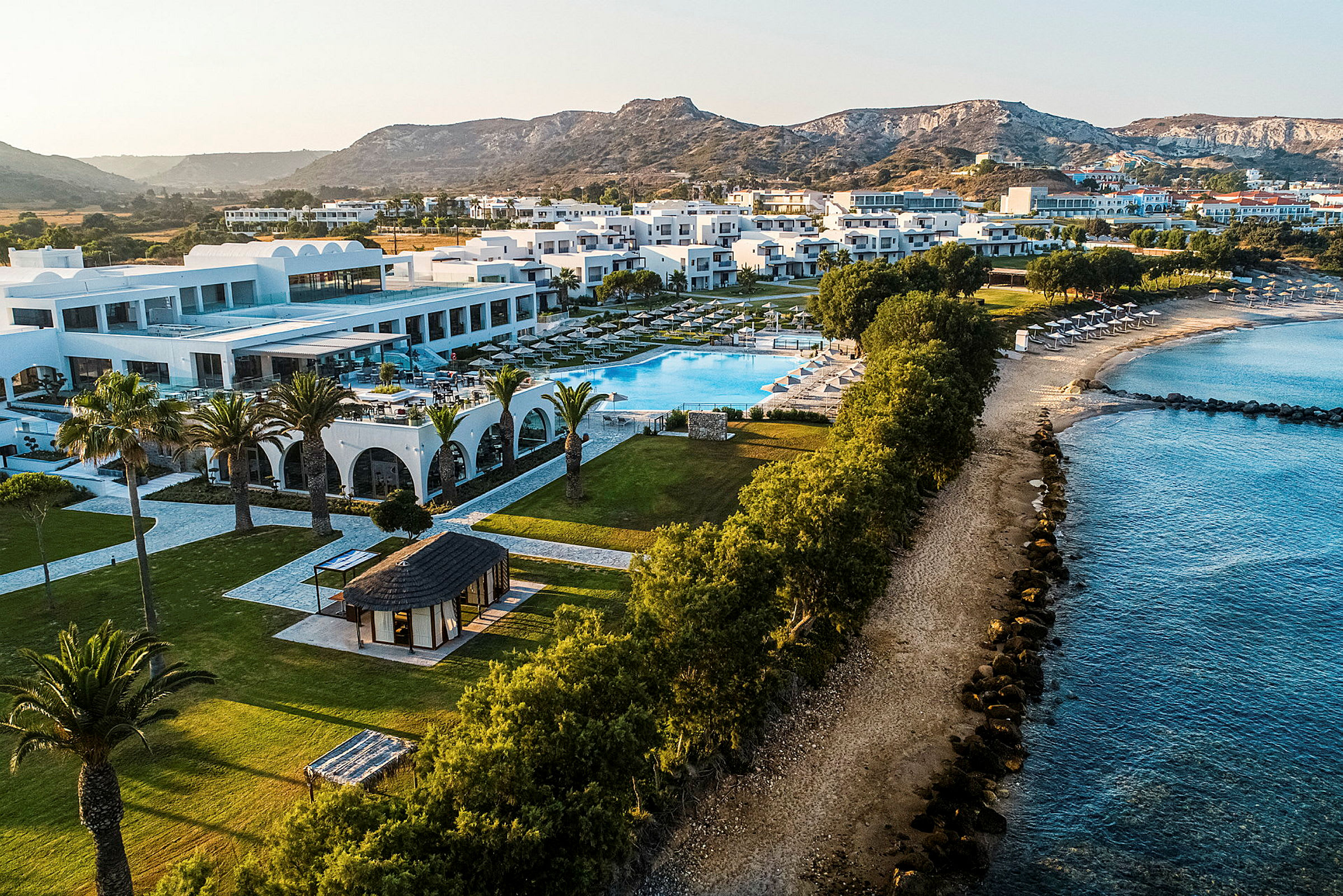 Vy över hotellkomplex med pool och strand på en sydlig solig semesterort. (AI-genererad text)