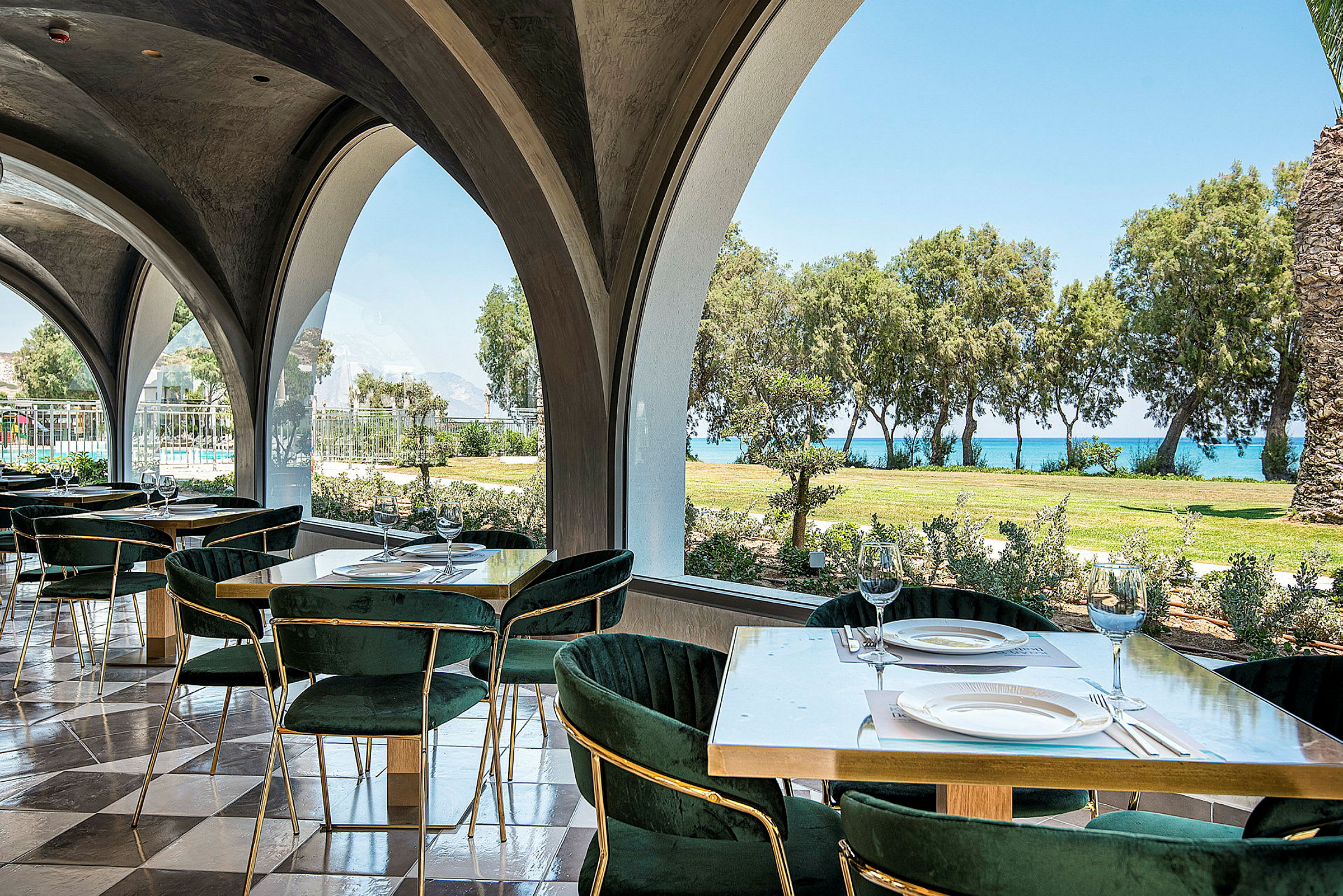 Restaurang med dukade bord och utsikt över trädgård och hav. (AI-genererad text)