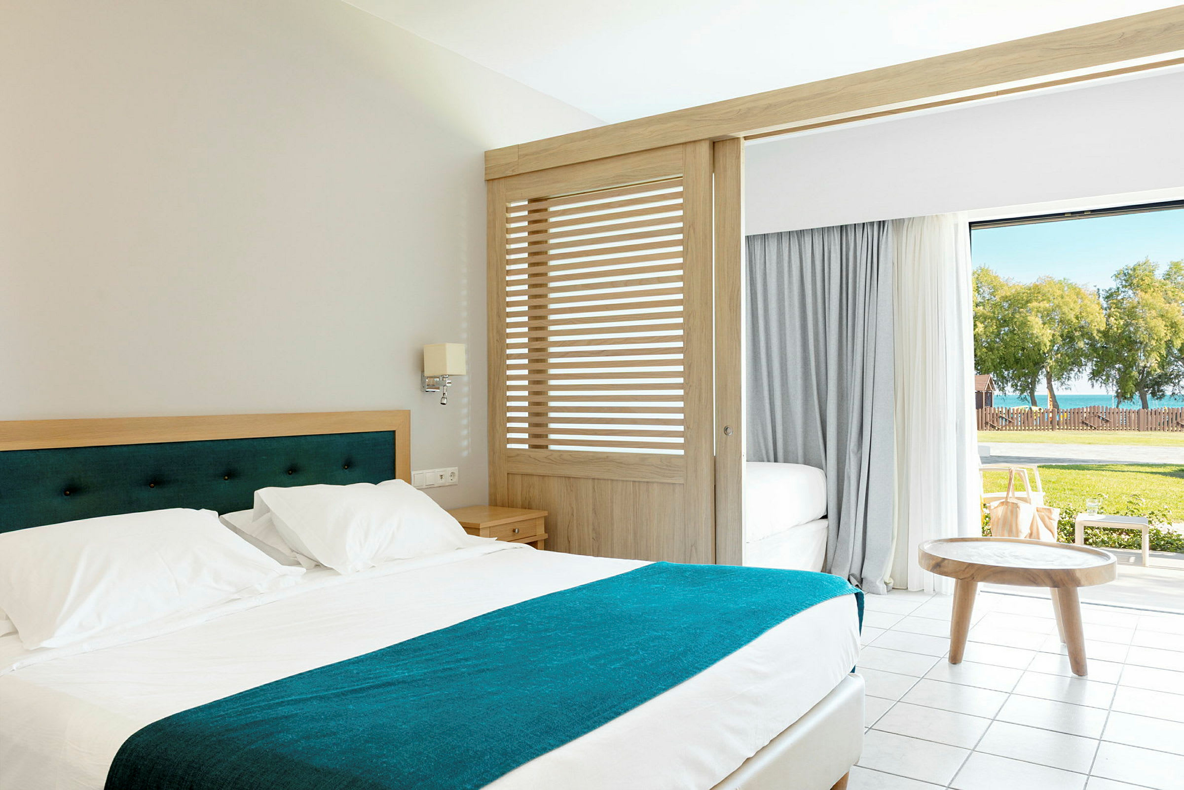 Ett hotellrum med en säng och öppningsbara dörrar som leder till en grönskande utomhusområde. (AI-genererad text)