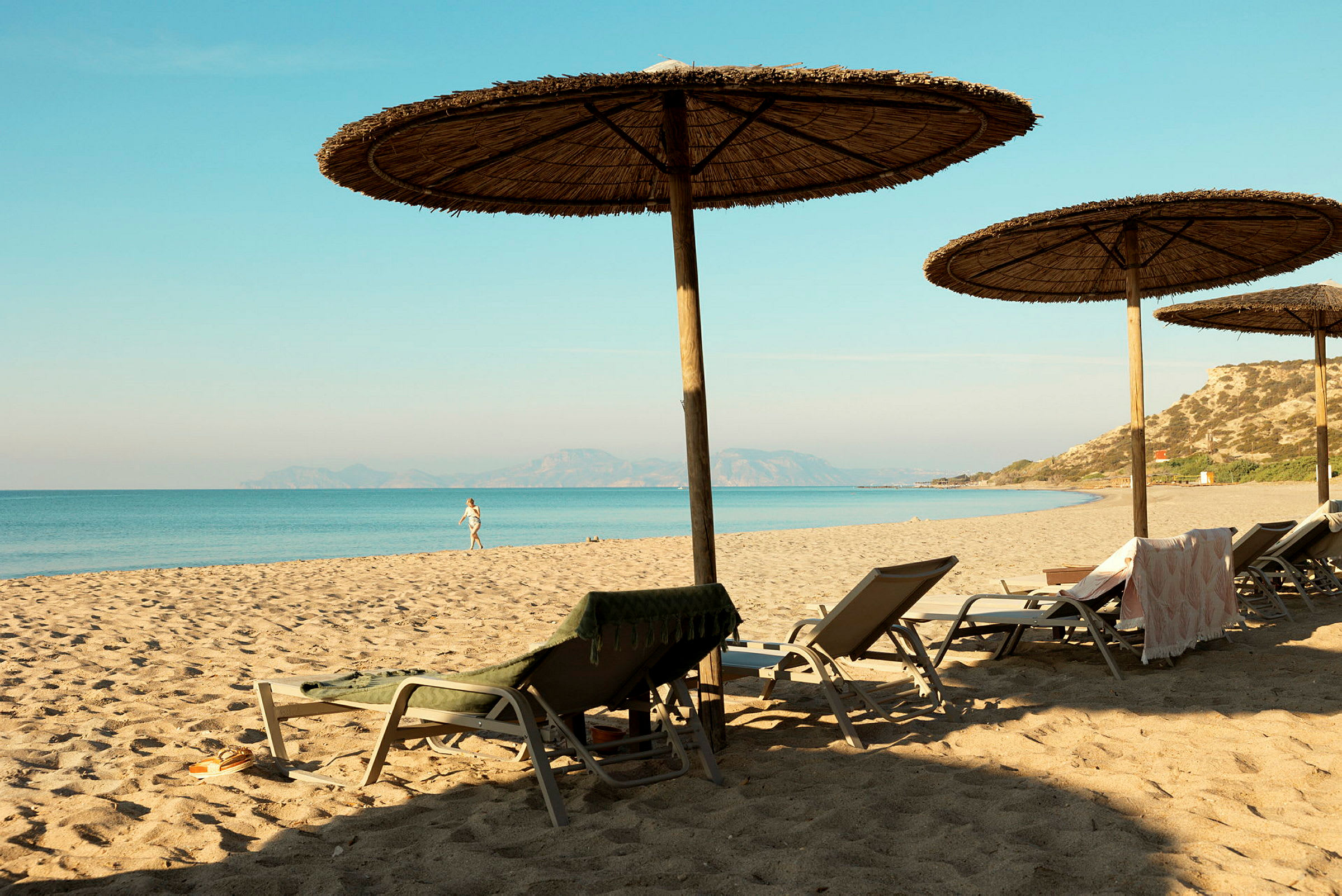 En sandstrand med parasoller och solstolar vid havet. (AI-genererad text)