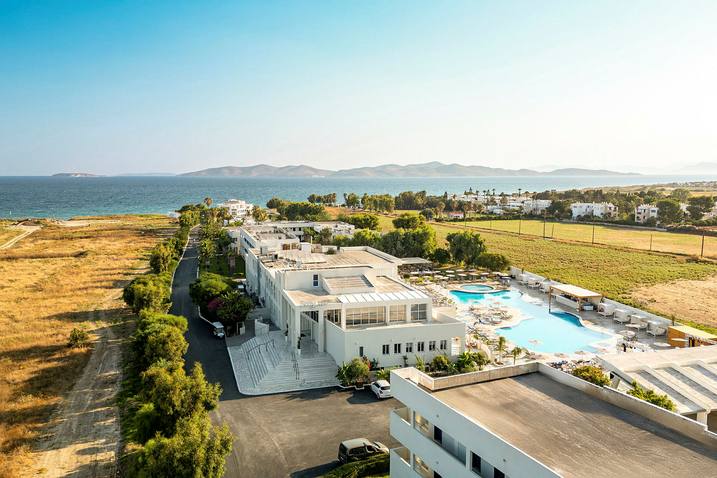Vy ovanifrån över en semesteranläggning nära havet med pool och grönområden. (AI-genererad text)