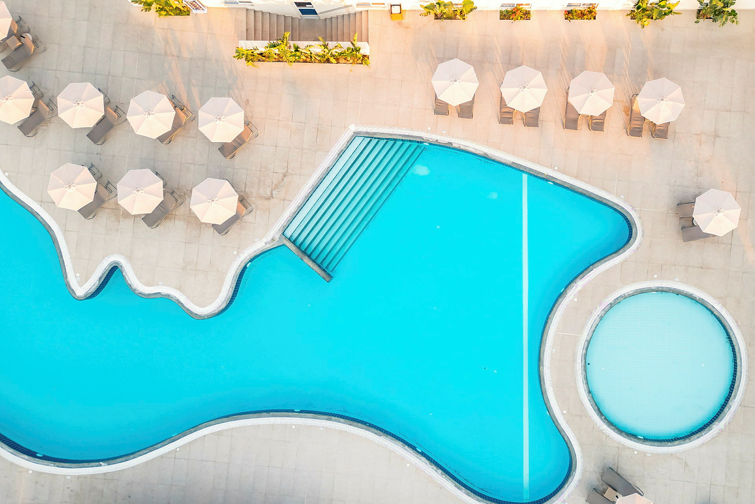 En pool med en liten rund barnpool bredvid och solstolar under parasoller på poolområdet. (AI-genererad text)