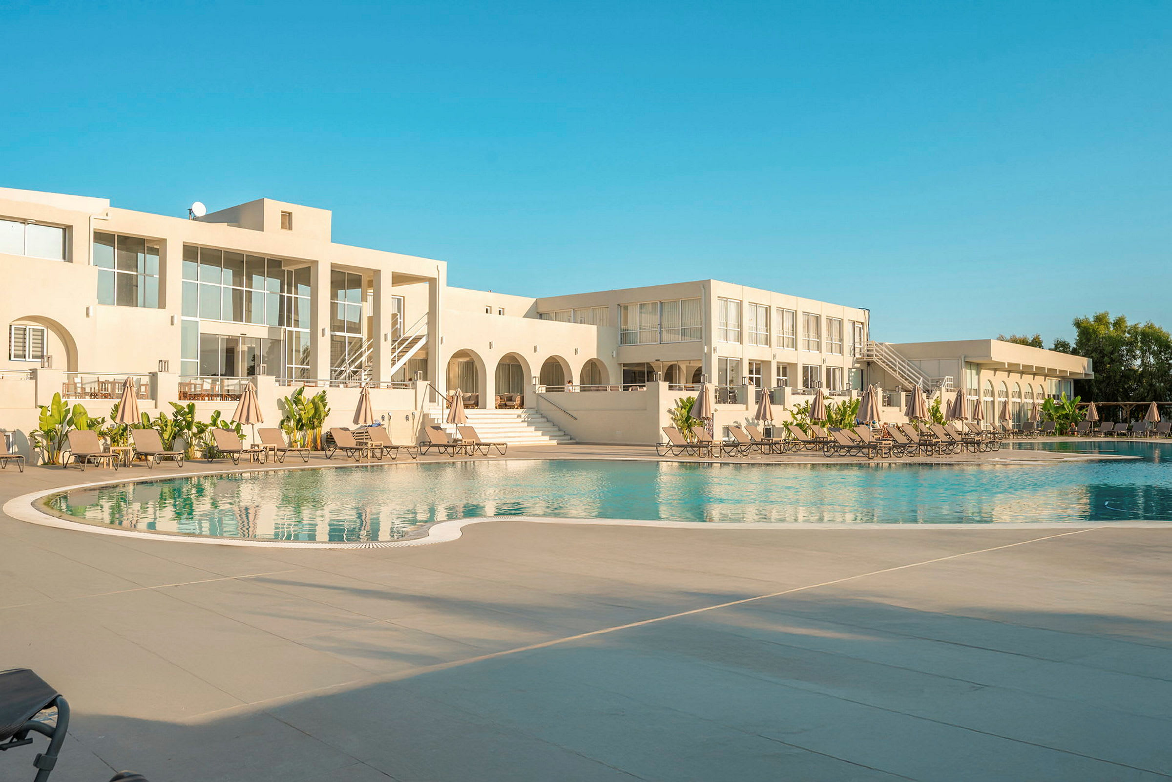 Hotellbyggnad med pool och solstolar. (AI-genererad text)