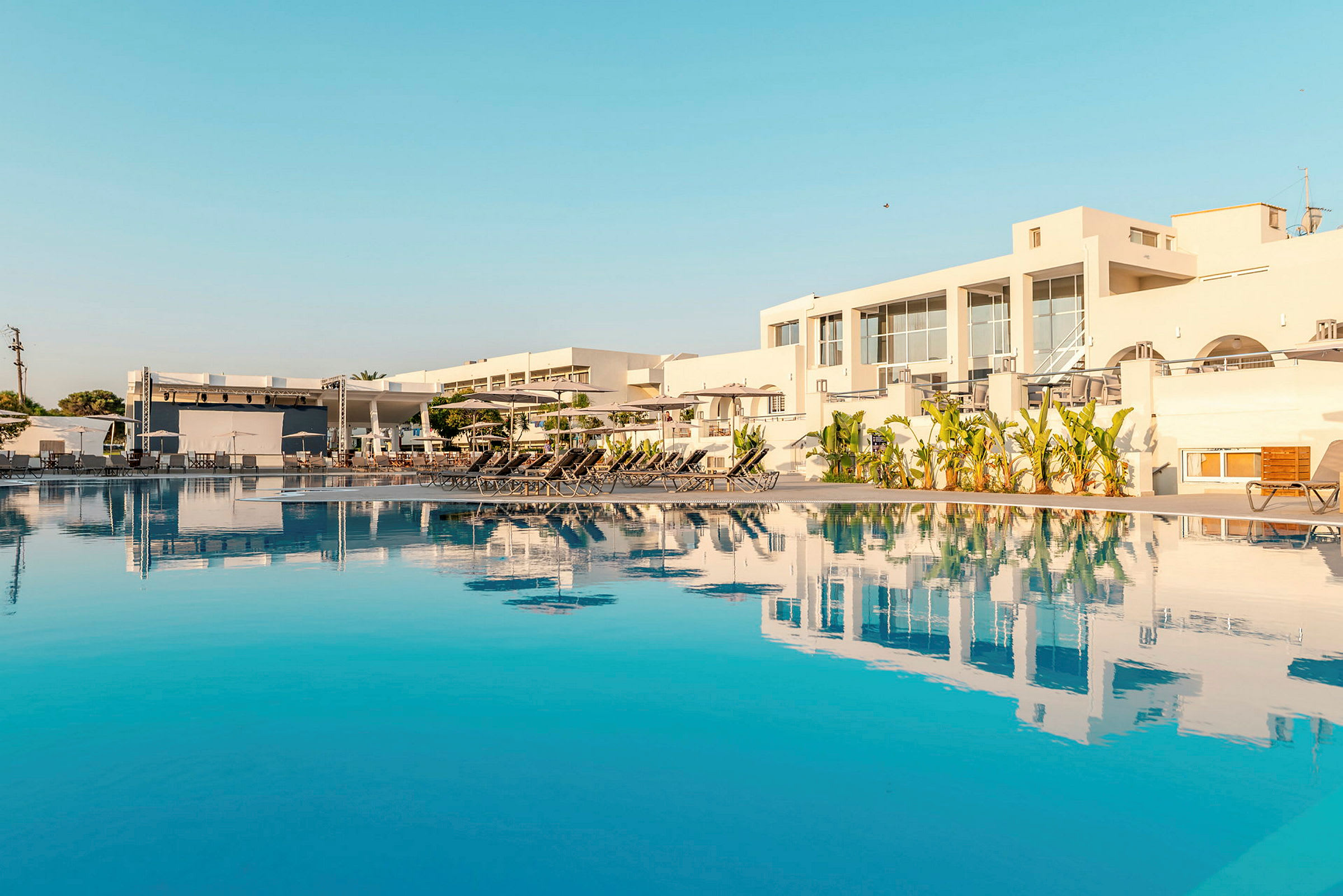 Stort poolområde med solstolar och modern vit hotellbyggnad. (AI-genererad text)