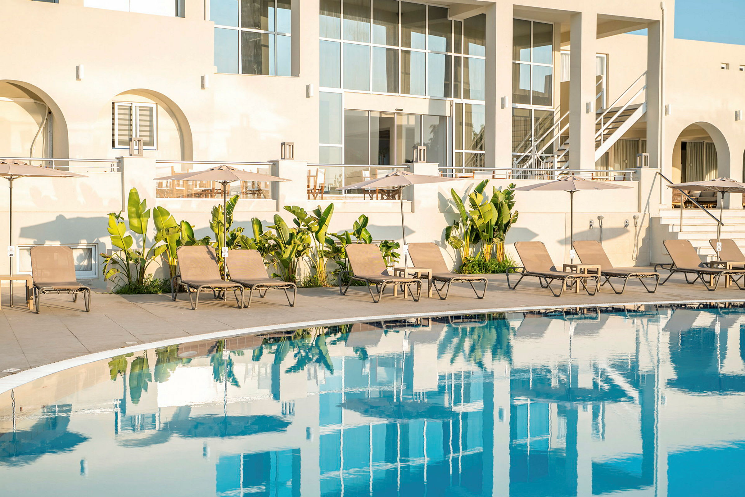 Bilden visar en pool framför ett hotell med solstolar och parasoll. (AI-genererad text)