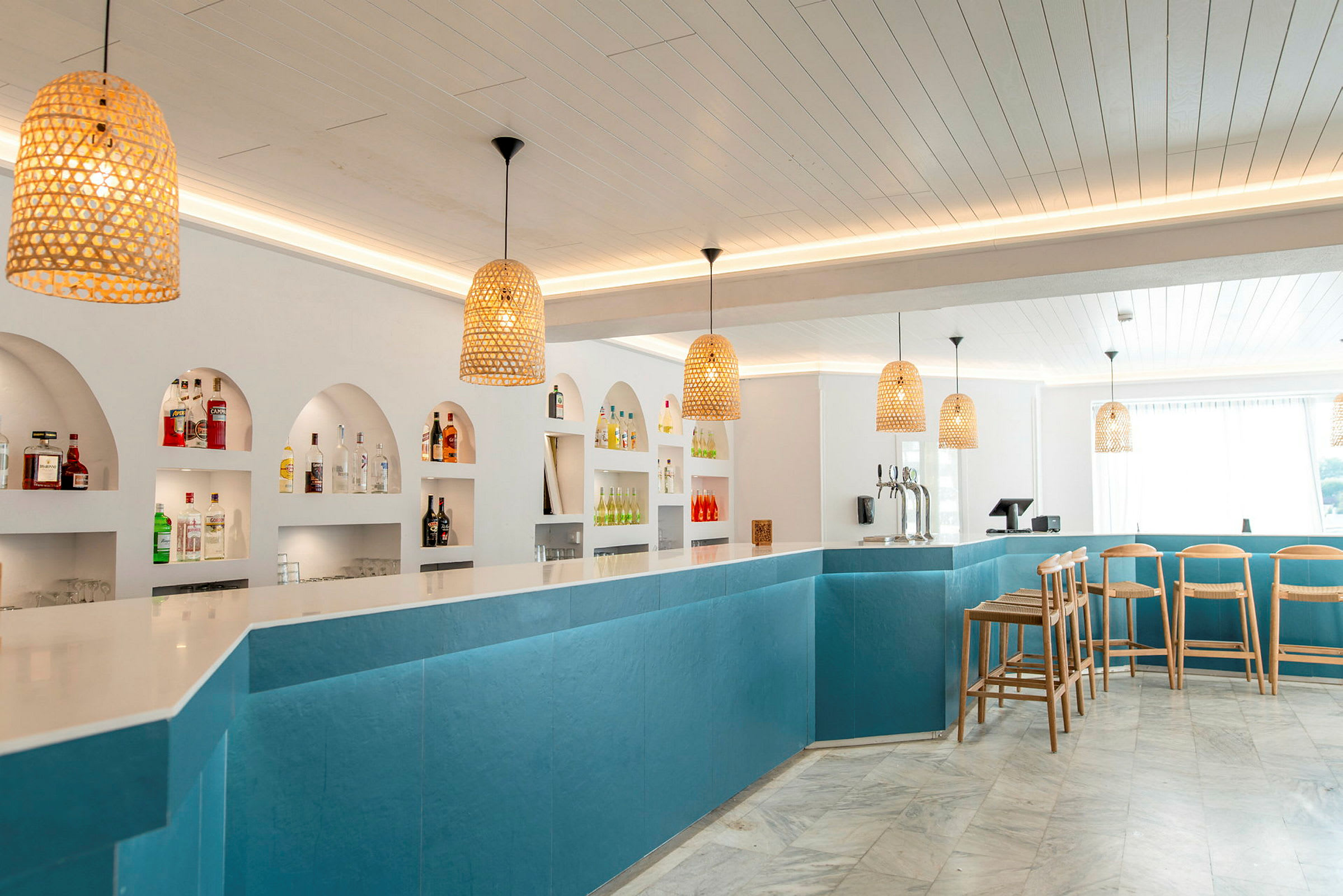 En modern bar med blå paneler, bordsskiva i vitt och ett antal flaskor på hyllor bakom. (AI-genererad text)