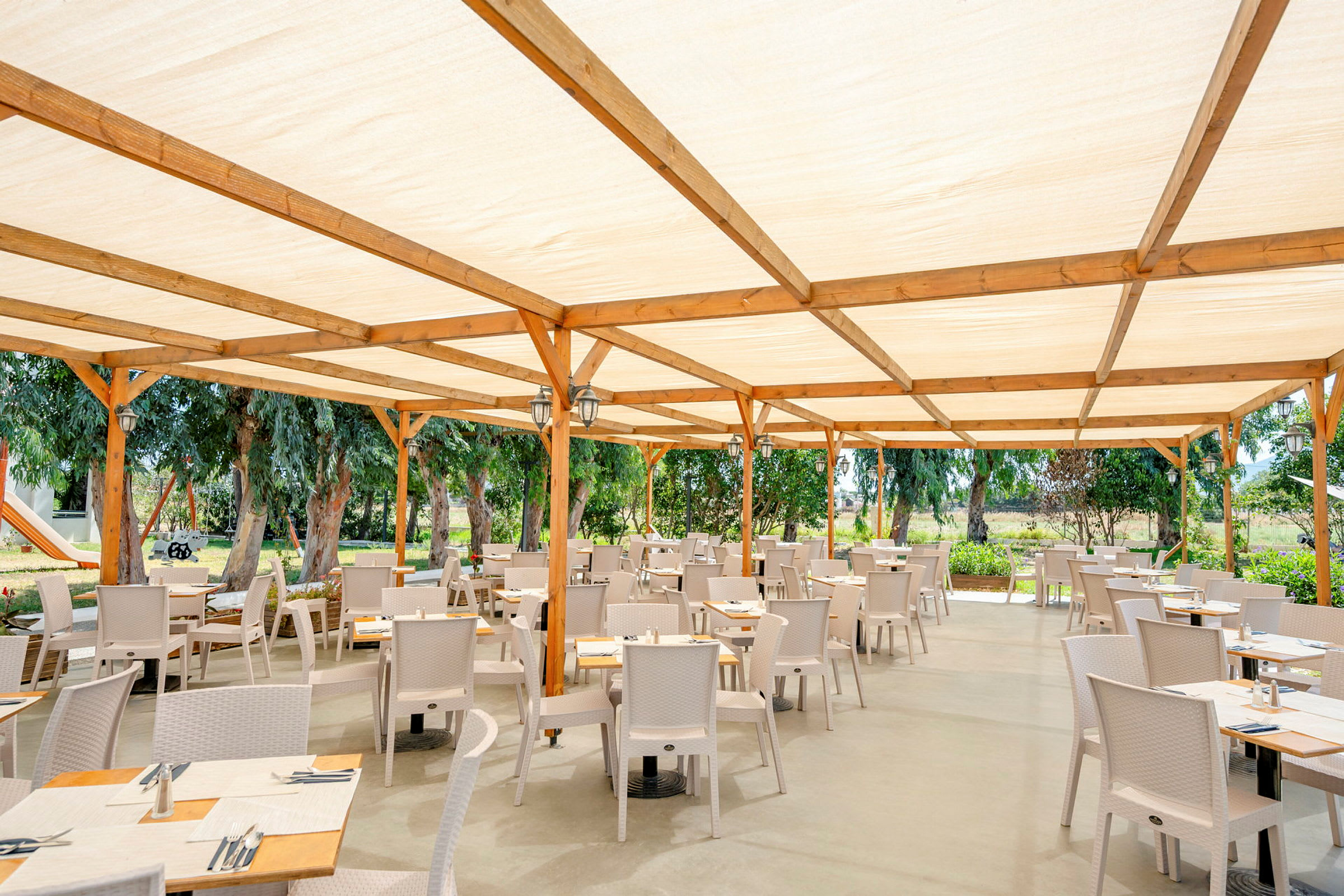En utomhusrestaurang med träställning och ljus takduk, omgiven av grönska. (AI-genererad text)