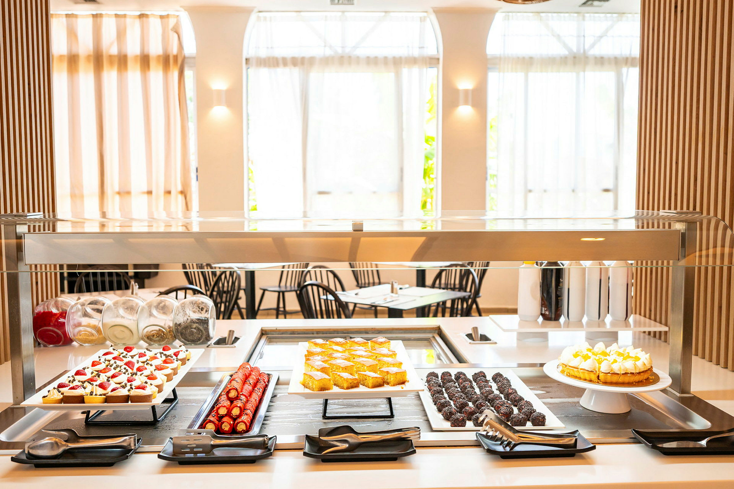 Ett dessertbord med olika bakverk och kakor under en glasskydd. (AI-genererad text)