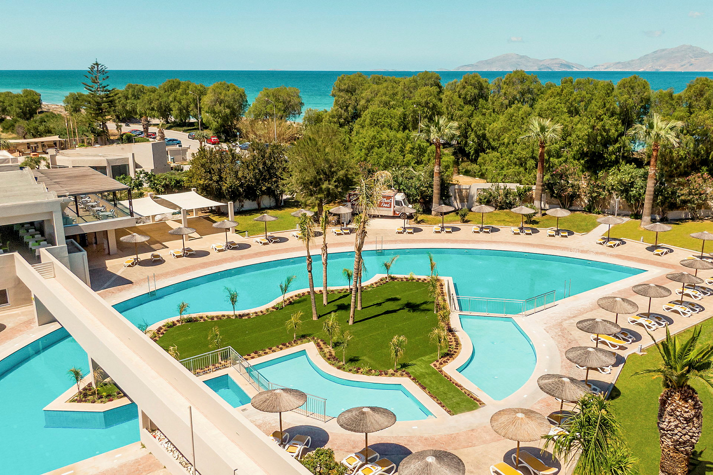 En hotellpool med solstolar och parasoller, omgiven av träd och med havsutsikt. (AI-genererad text)