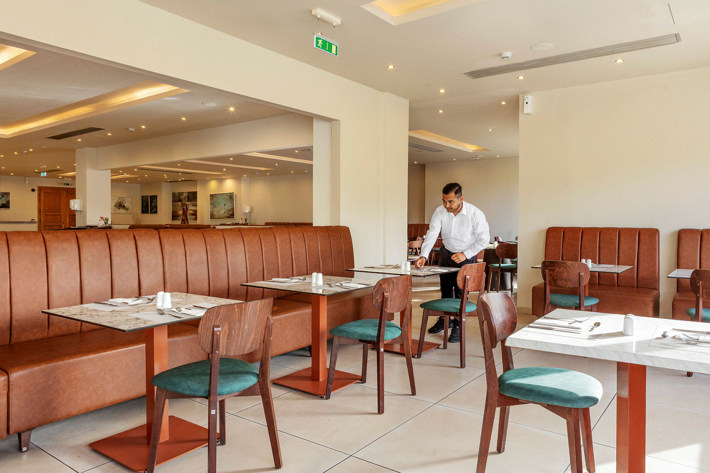 Interiör av en restaurang med bord och stolar samt en brun lädersoffa. (AI-genererad text)