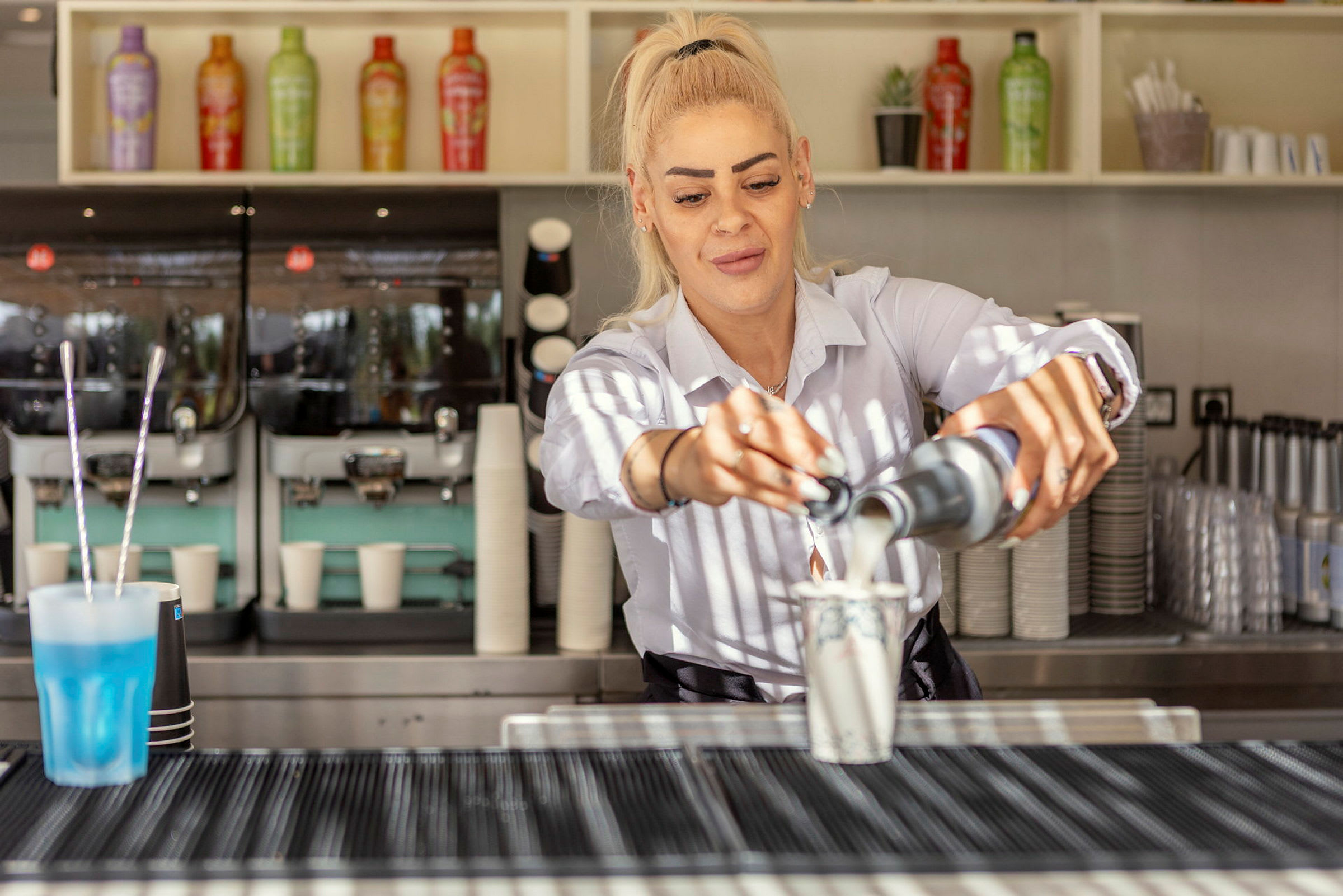 Person häller upp en vätska i en kopp bakom en kaffebar. (AI-genererad text)