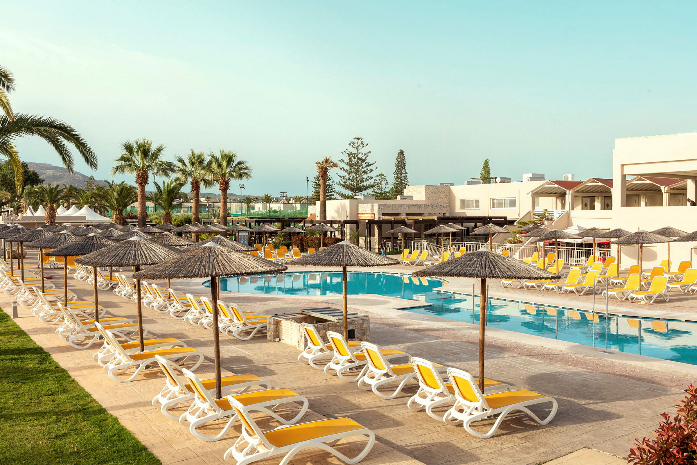 Solstolar och parasoller kring hotellpool med palmer och byggnader i bakgrunden. (AI-genererad text)