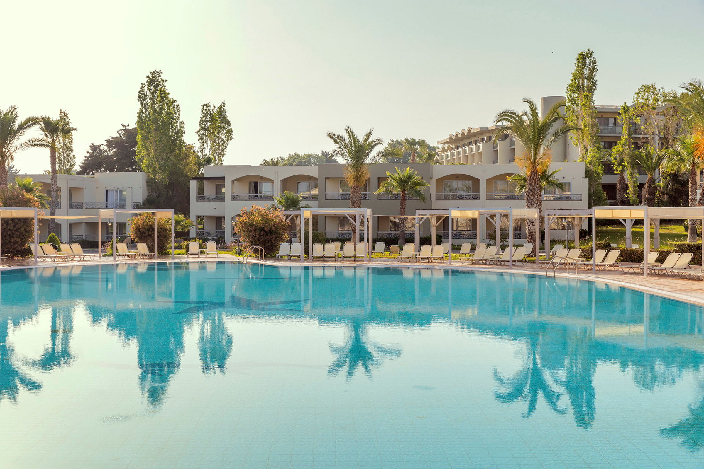 En utomhuspool framför hotellbyggnader och palmer. (AI-genererad text)