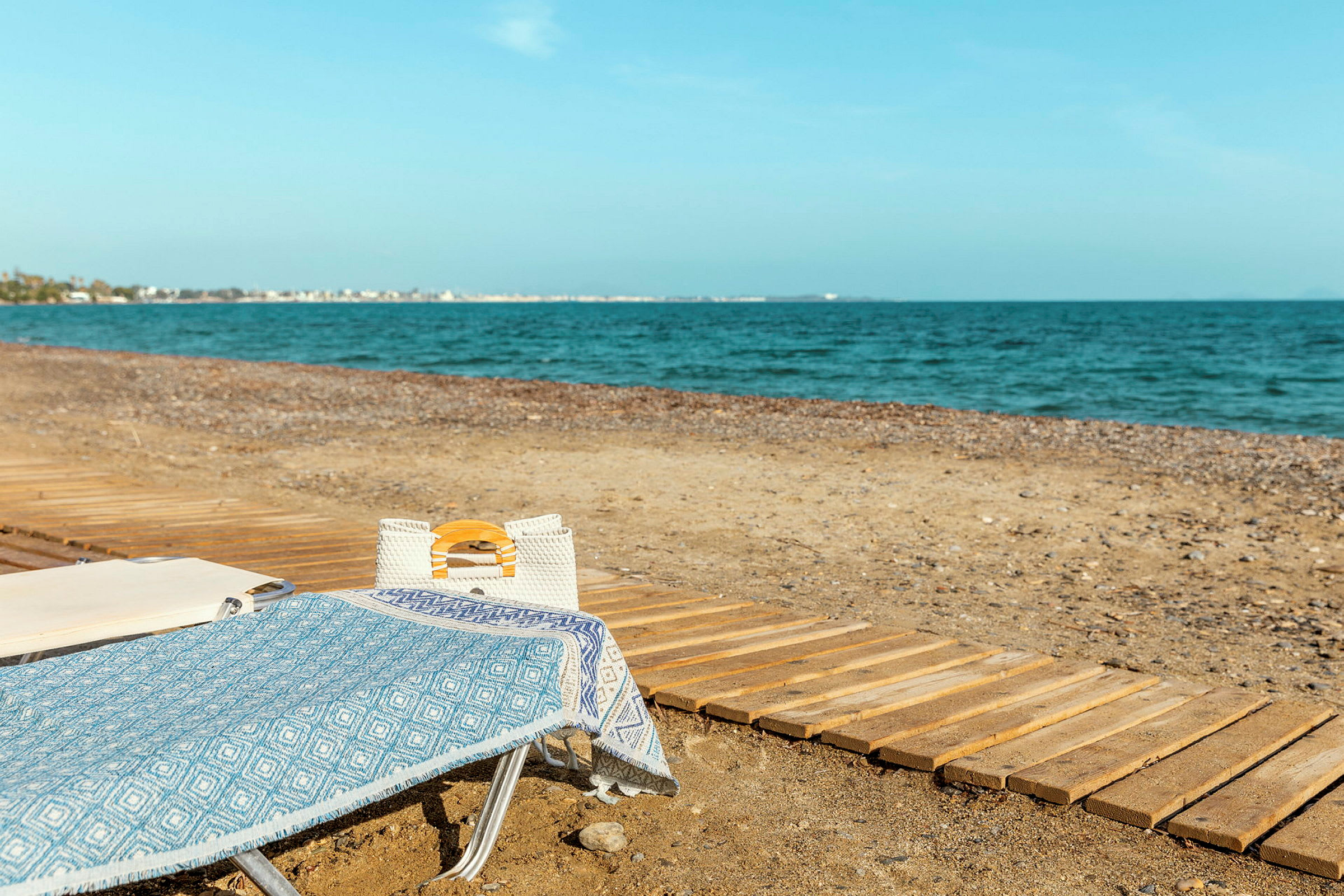 Solstol med blå handduk och vit väska på en strand vid havet. (AI-genererad text)