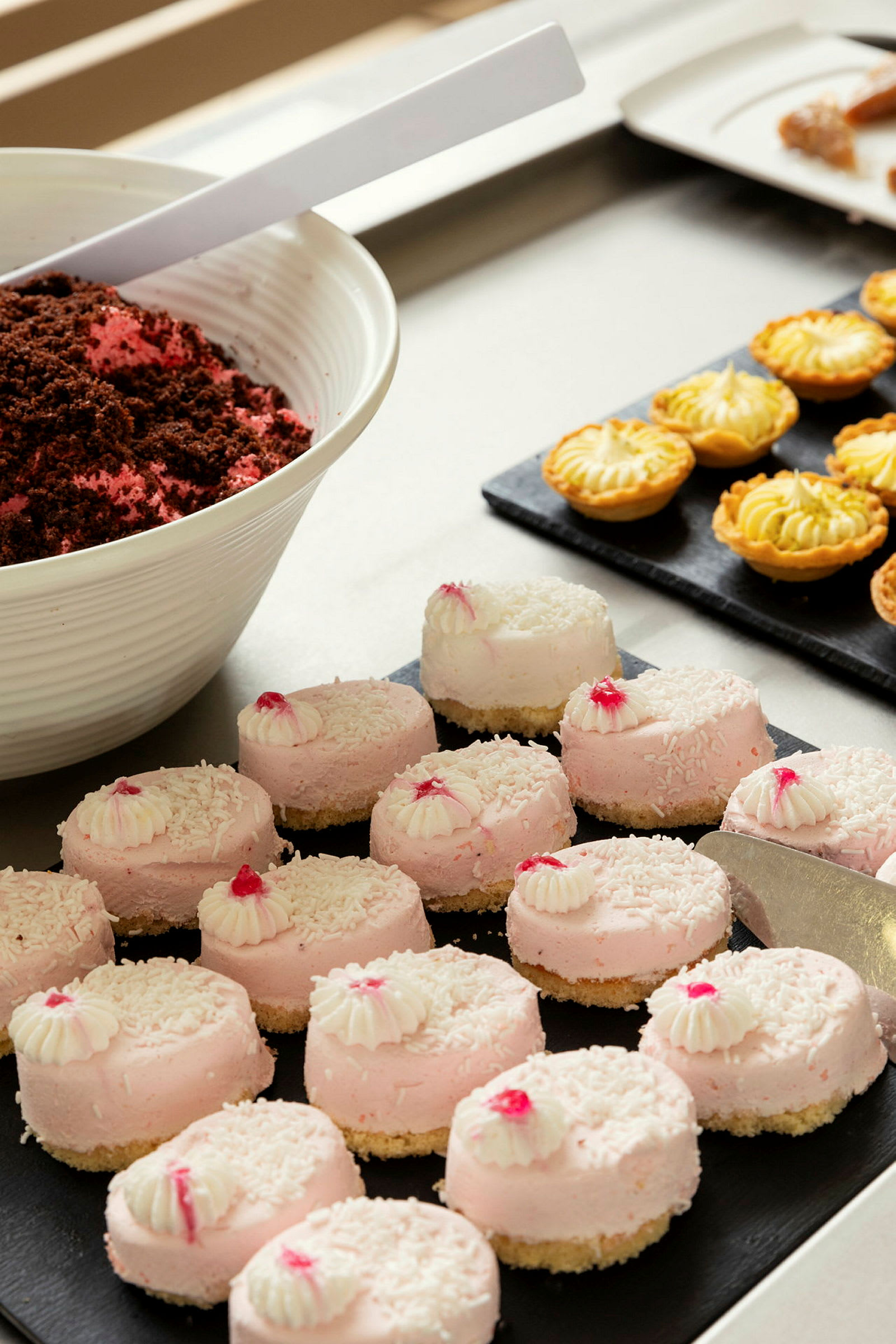 Rosa desserter med kokos och vit topping, samt små pajer i bakgrunden. (AI-genererad text)