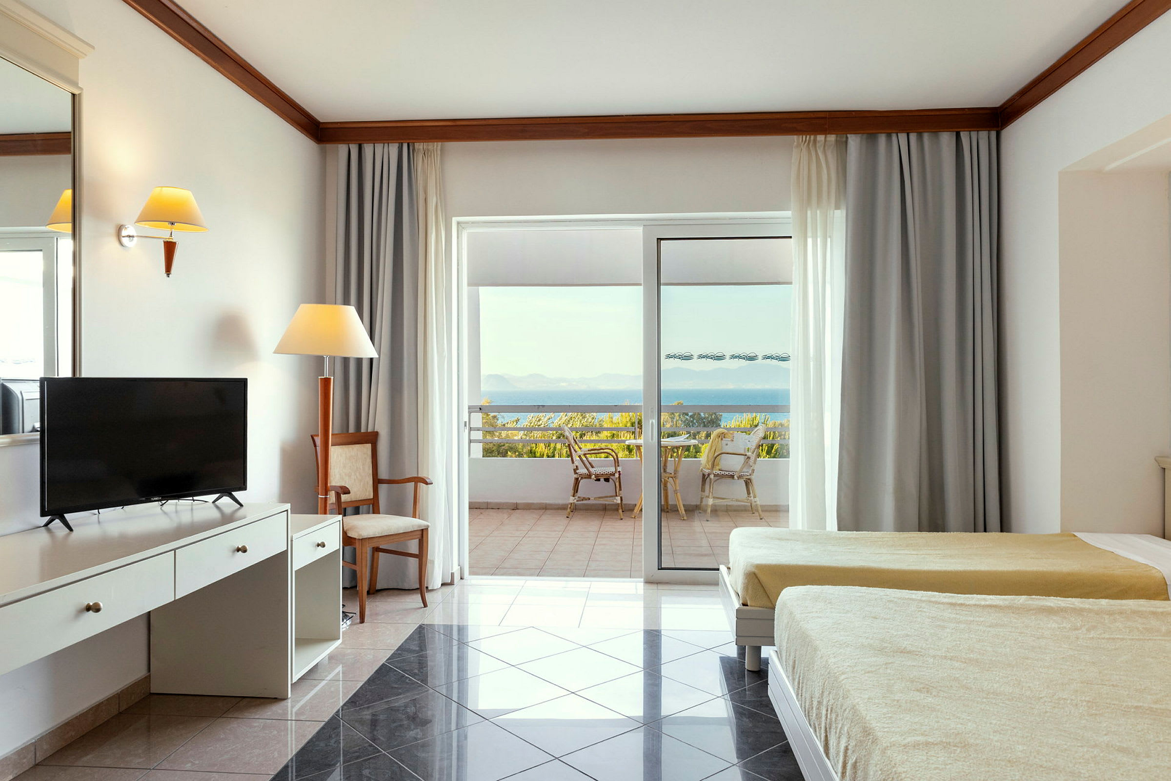 Interiör av ett hotellrum med två sängar, skrivbord och en uteplats med utsikt över havet. (AI-genererad text)