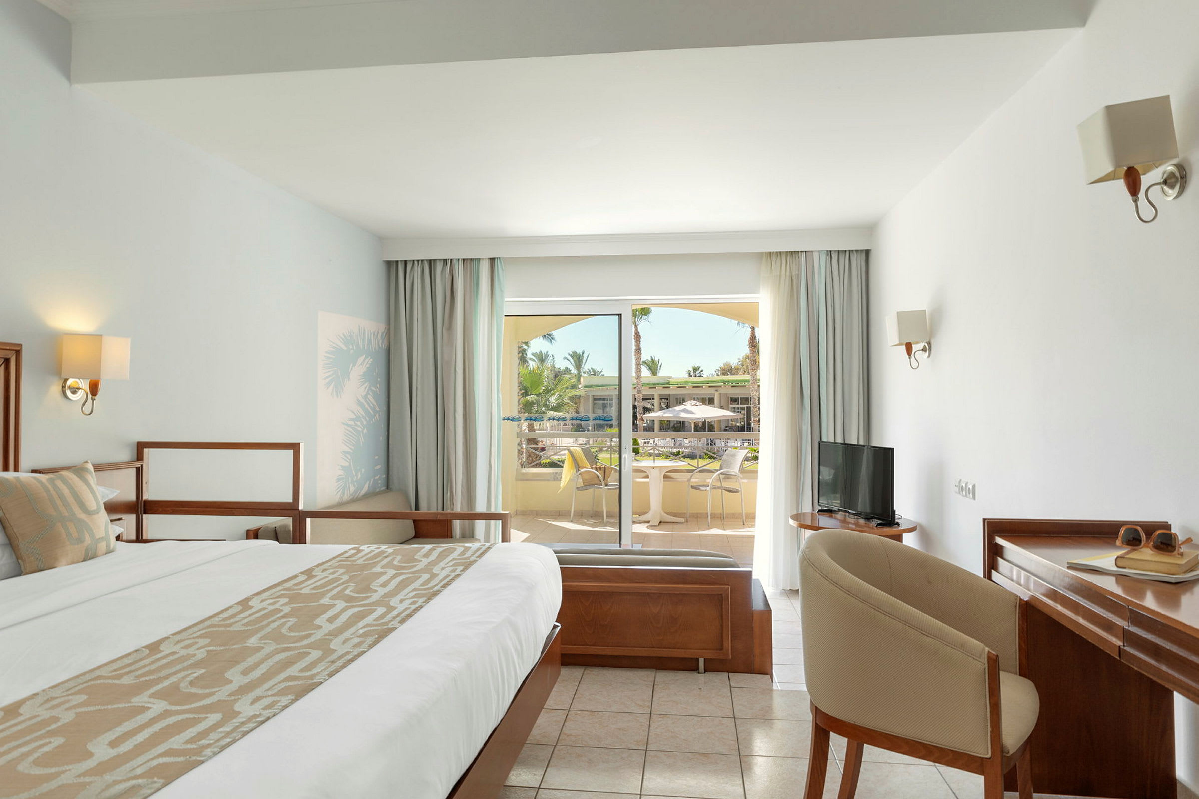 Hotellrum med moderne inredning, stor säng, skrivbord och utsikt över en terrass. (AI-genererad text)