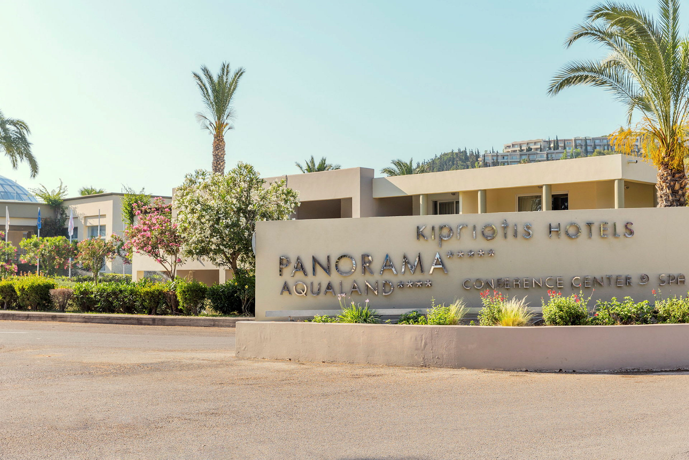 Hotellskylt med texten 'Kipriotis Hotels Panorama Aqualand Conference Center & Spa', omgiven av grönska och palmer. (AI-genererad text)