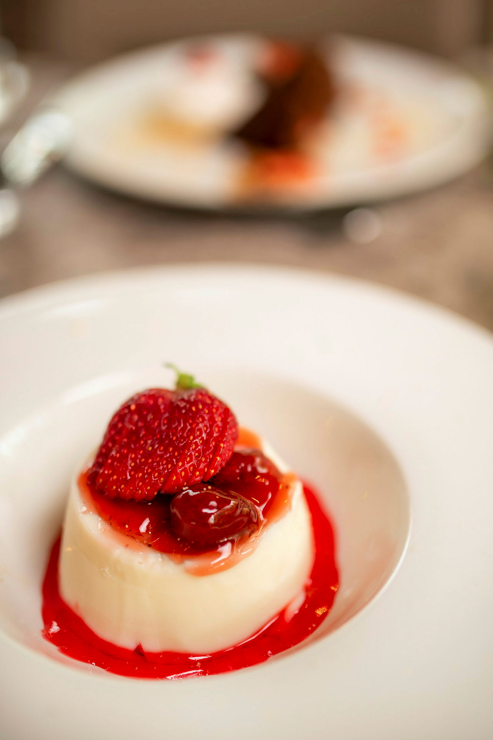 En dessert med vaniljpudding toppad med jordgubbar och frukt i en röd sås på en vit tallrik. (AI-genererad text)