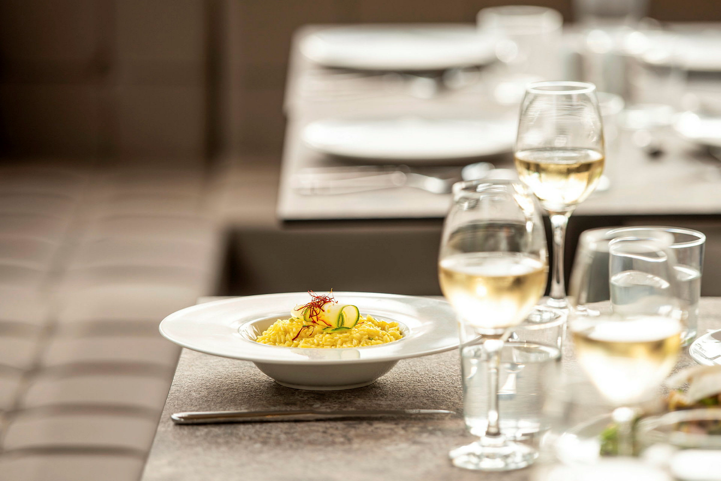 En tallrik risotto och ett glas vitt vin på ett dukat bord. (AI-genererad text)