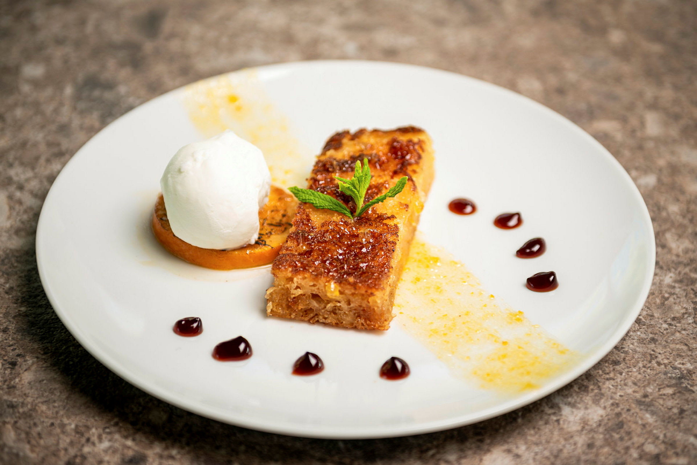 En tallrik med en dessert bestående av karamelliserat bröd, grädde och garnering. (AI-genererad text)