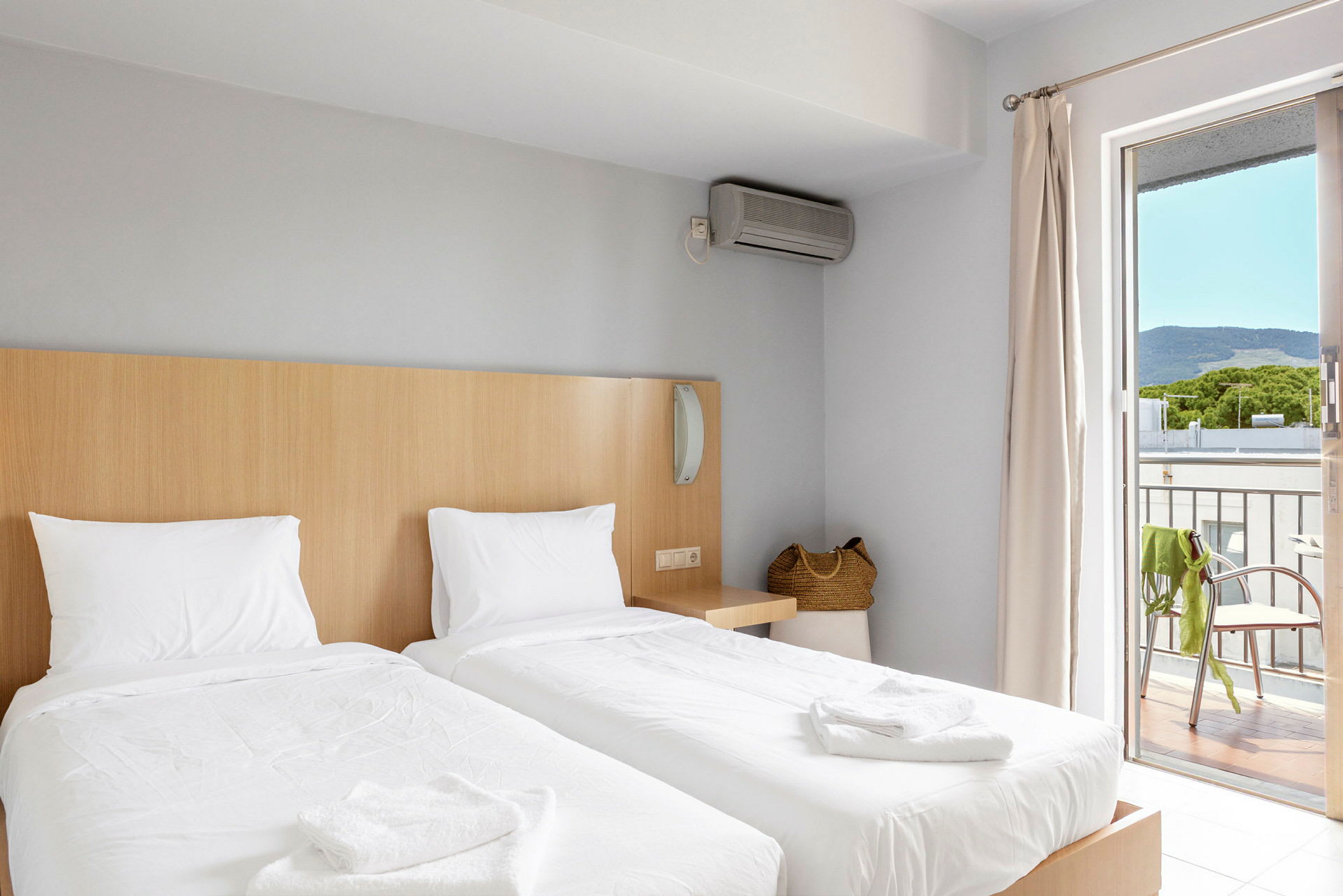 Ett hotellrum med två enkelsängar, en basket handväska, och en balkong med utsikt. (AI-genererad text)