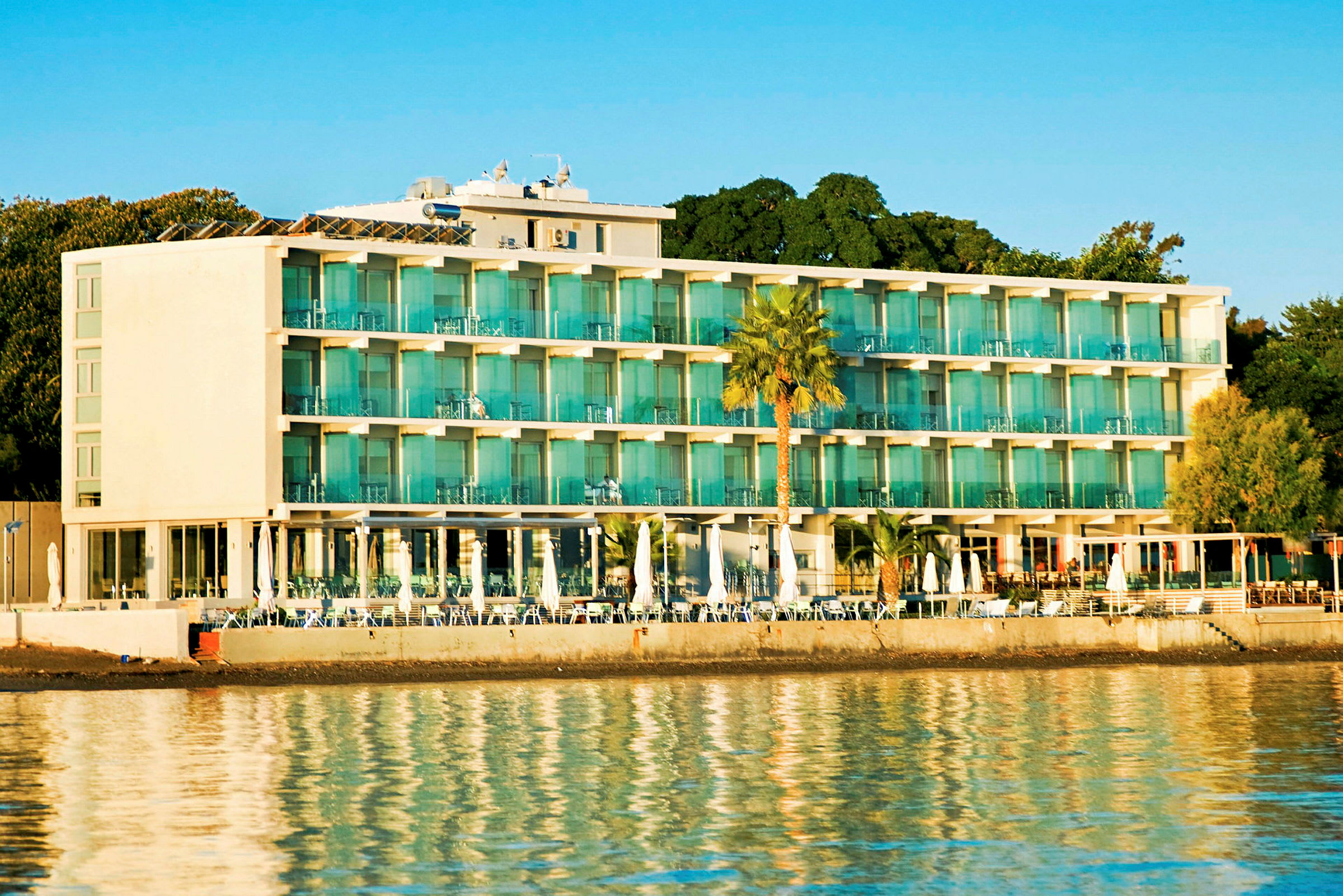 Modern hotellbyggnad vid vattnet, omgiven av grönska. (AI-genererad text)