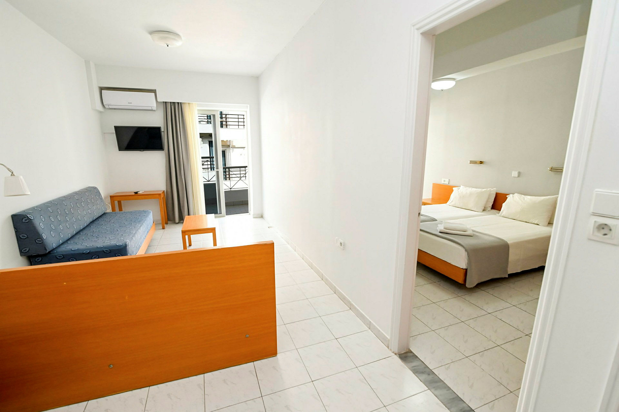 Ett hotellrum med en vardagsrumsdel innehållande en blå soffa och bord samt en sovrumsdel med en dubbelbädd. (AI-genererad text)