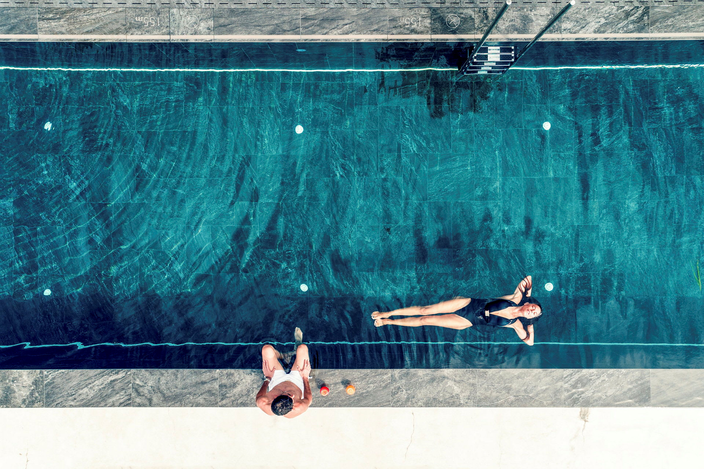 Person badar i en pool bredvid någon som sitter på kanten. (AI-genererad text)