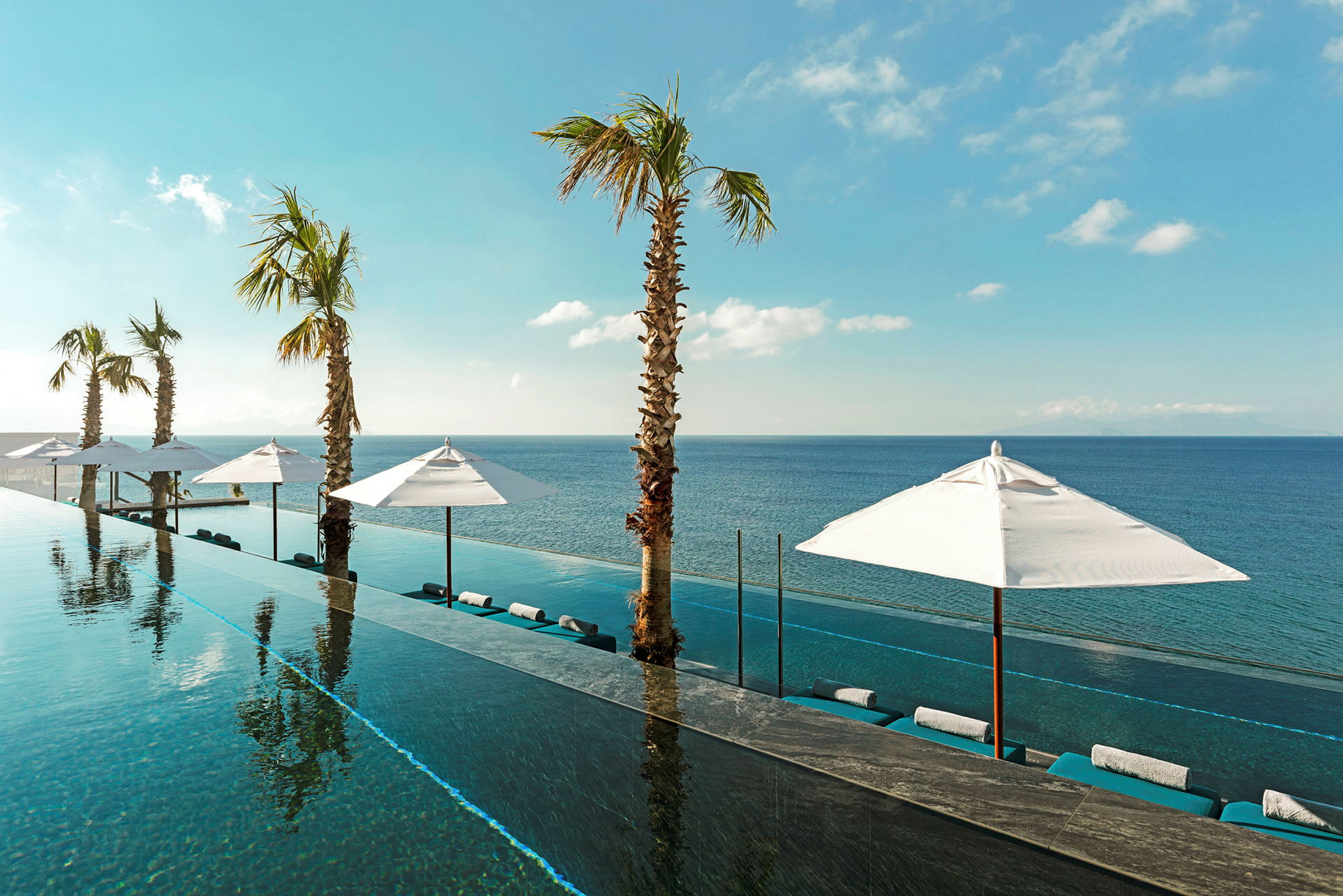 En infinitypool med utsikt mot havet, omgiven av solparasoller och palmer under en klarblå himmel. (AI-genererad text)