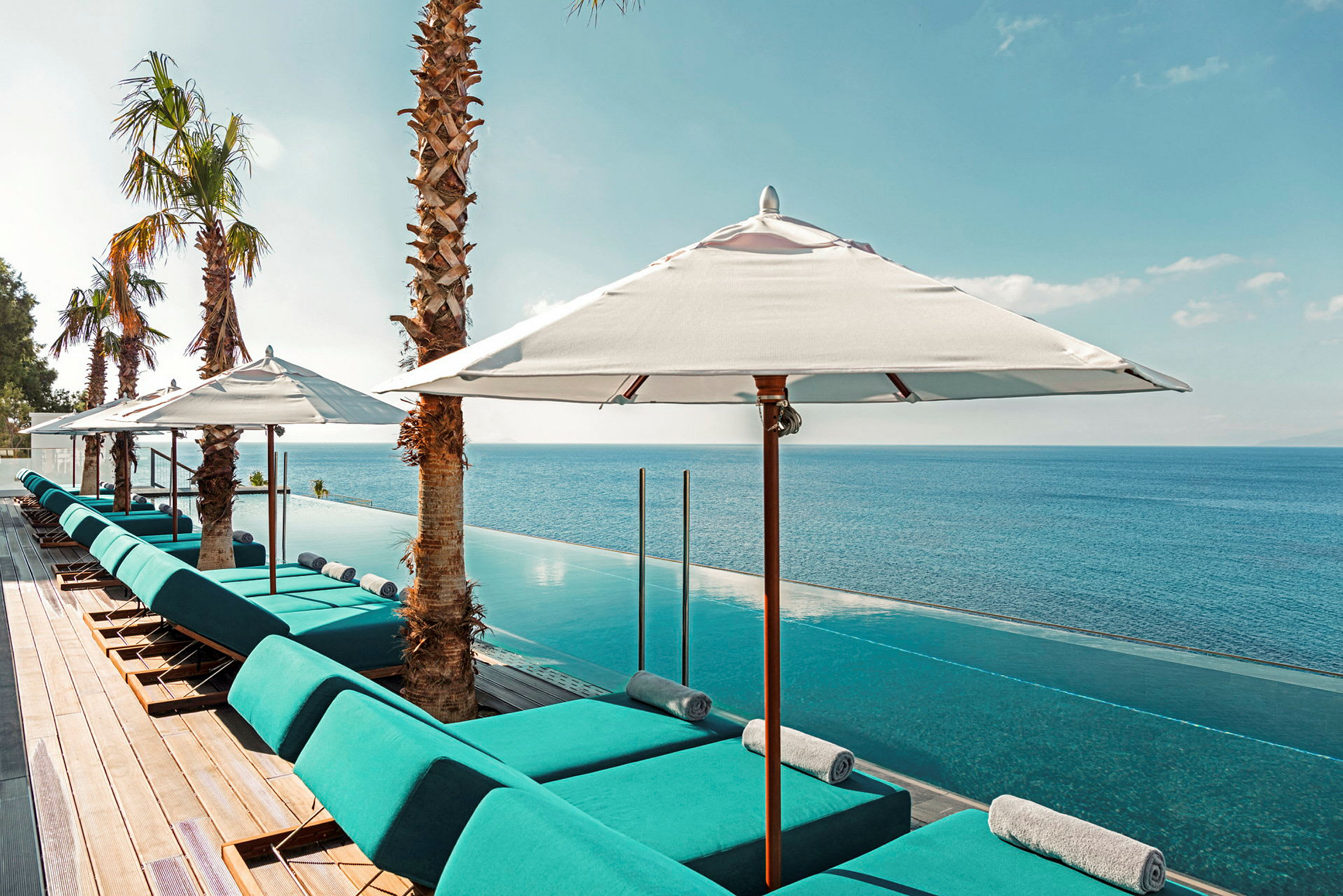 En infinitypool med blå solstolar under vita parasoller och utsikt över havet. (AI-genererad text)