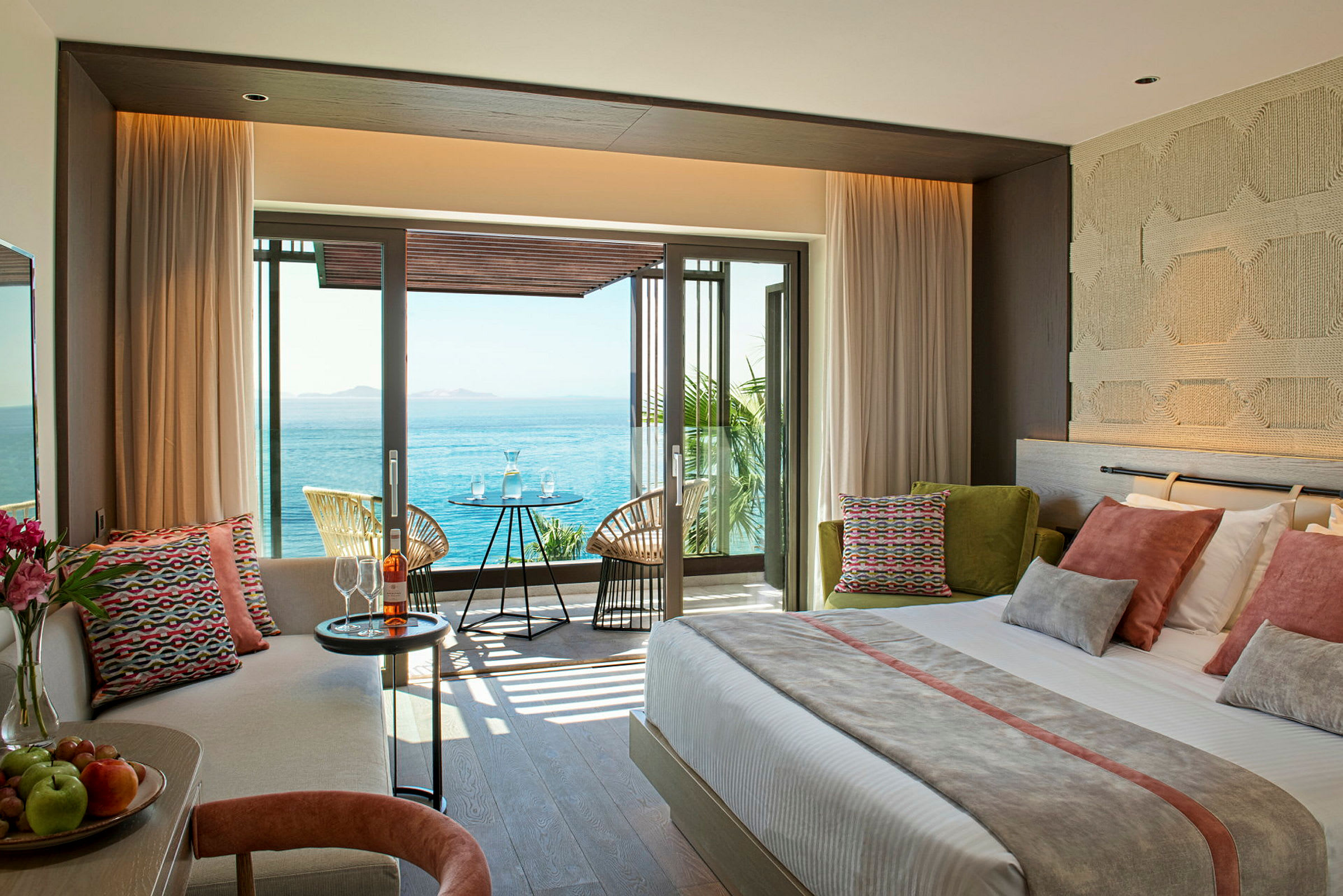 Bild på ett modernt hotellrum med utsikt mot havet genom stora fönster och en balkong med sittmöbler. (AI-genererad text)