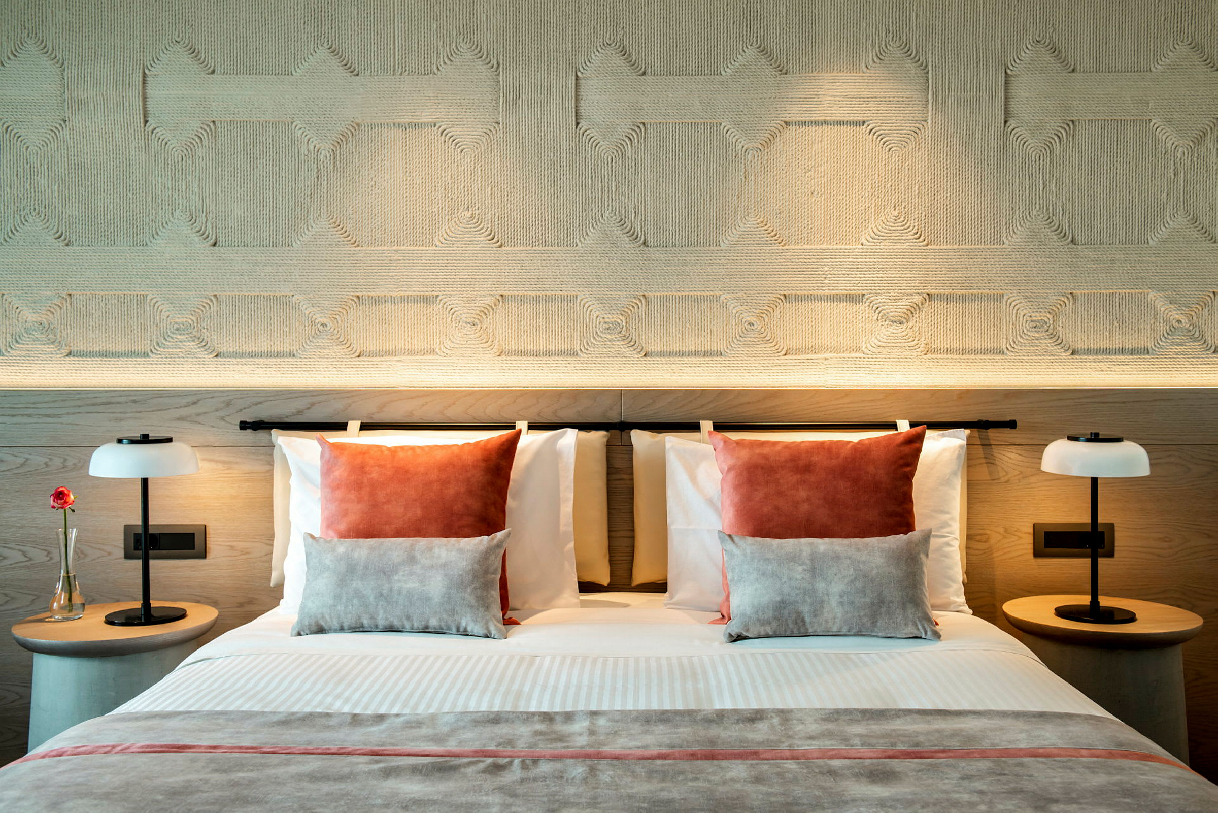 En modern hotellsäng med dekorativa kuddar och symmetriska nattduksbord prydda med lampor. (AI-genererad text)