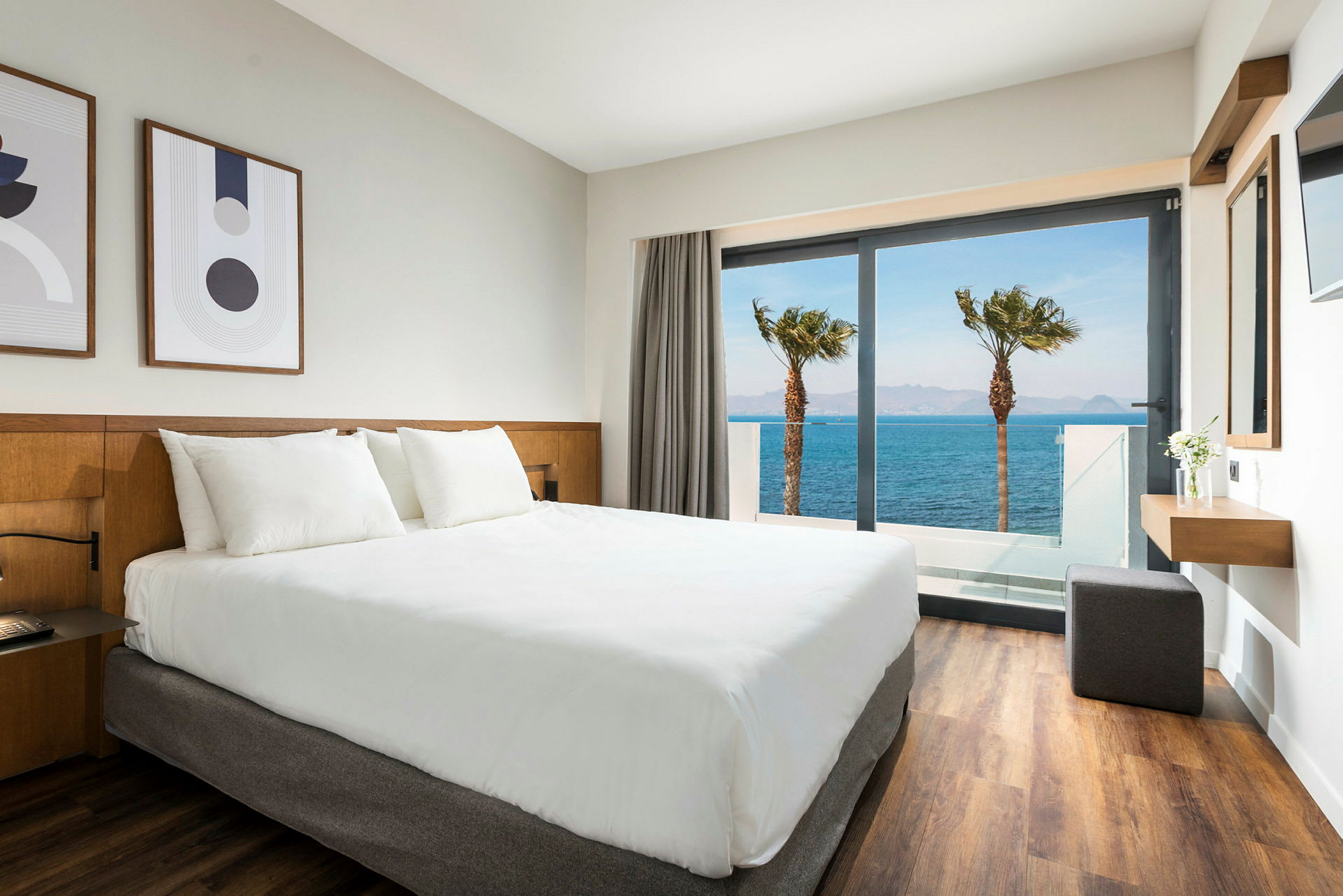 Hotellrum med vit säng och utsikt över havet genom en glasdörr. (AI-genererad text)