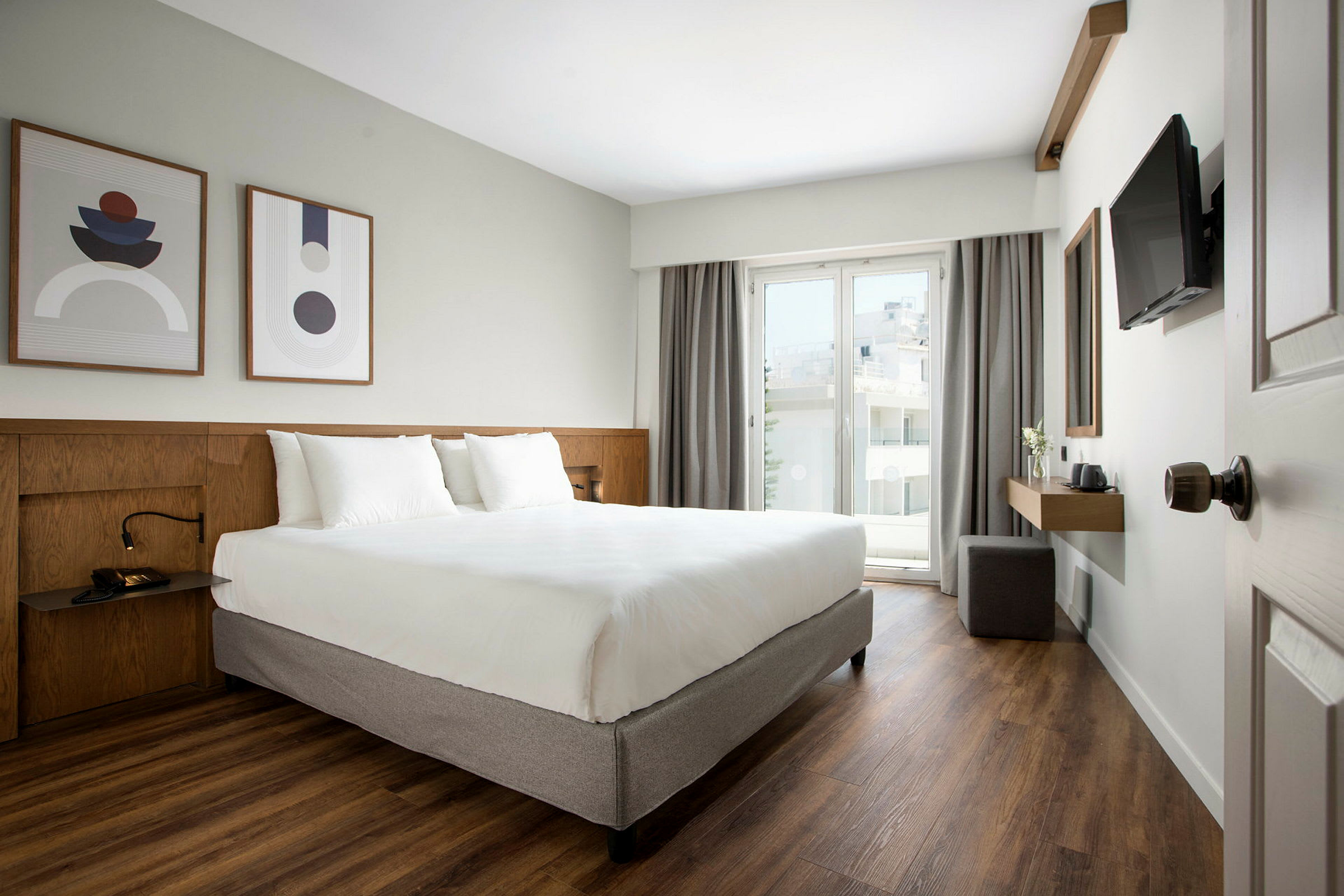 Modernt hotellrum med dubbelsäng, konst på väggen och balkong med glasdörr. (AI-genererad text)