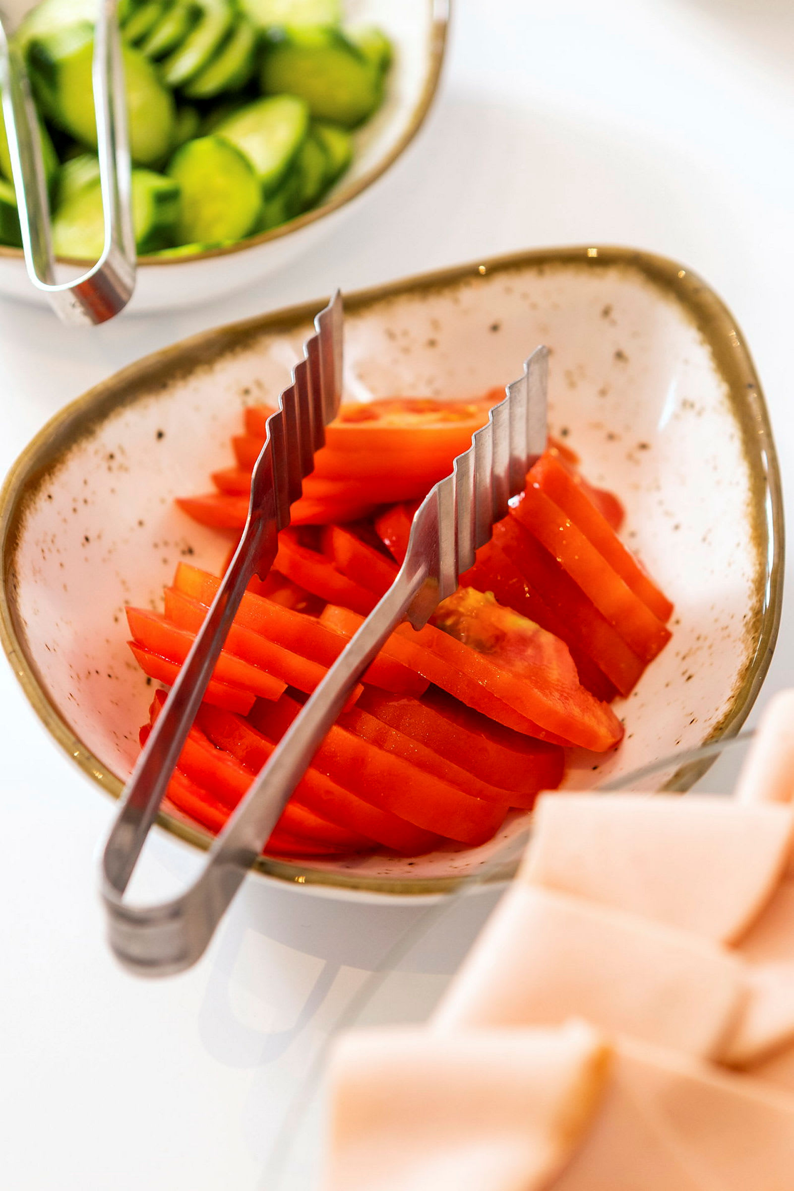 En skål med skivade tomater och tänger, omgiven av andra maträtter. (AI-genererad text)