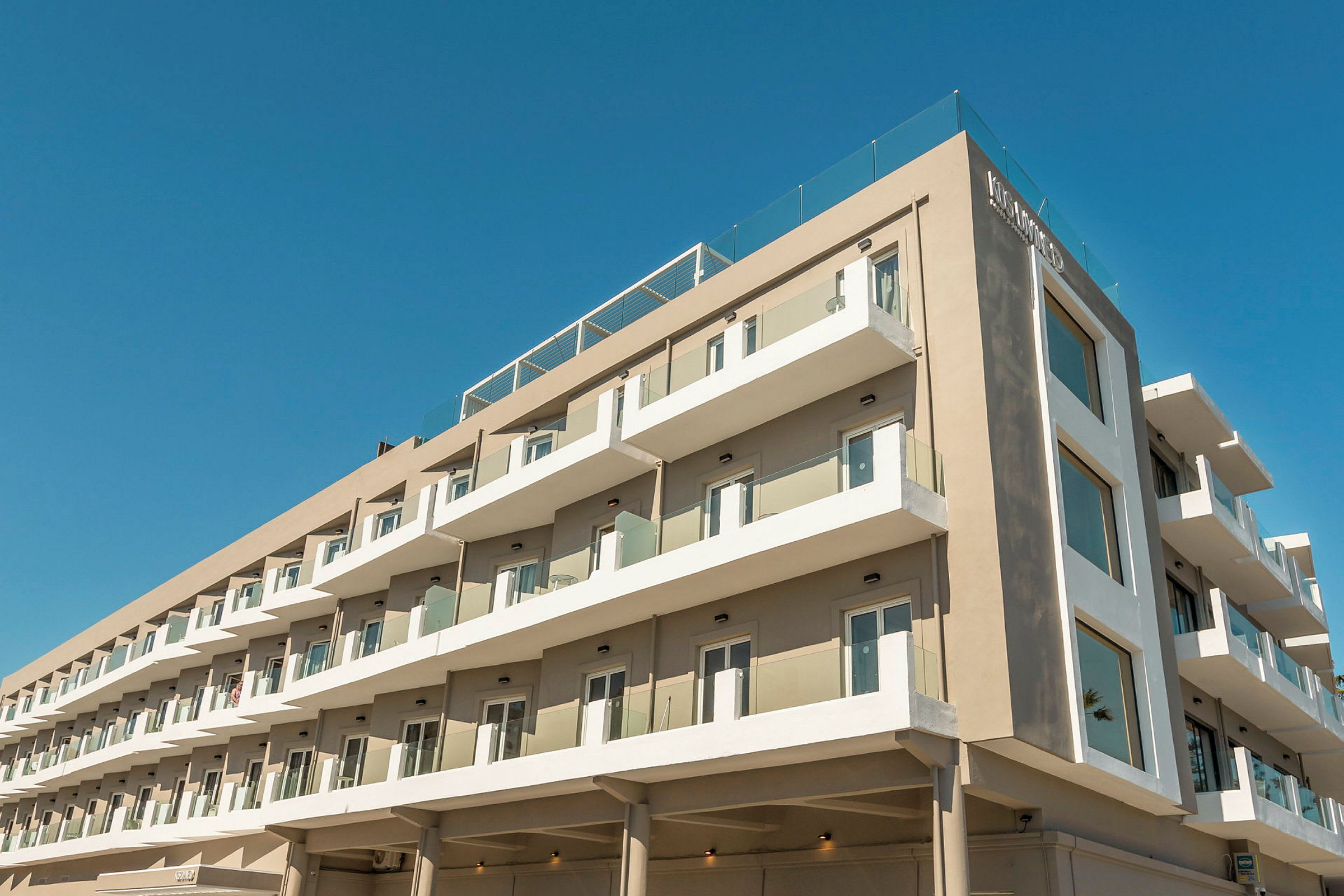 Modern hotellbyggnad med flera våningar och balkonger under en blå himmel. (AI-genererad text)