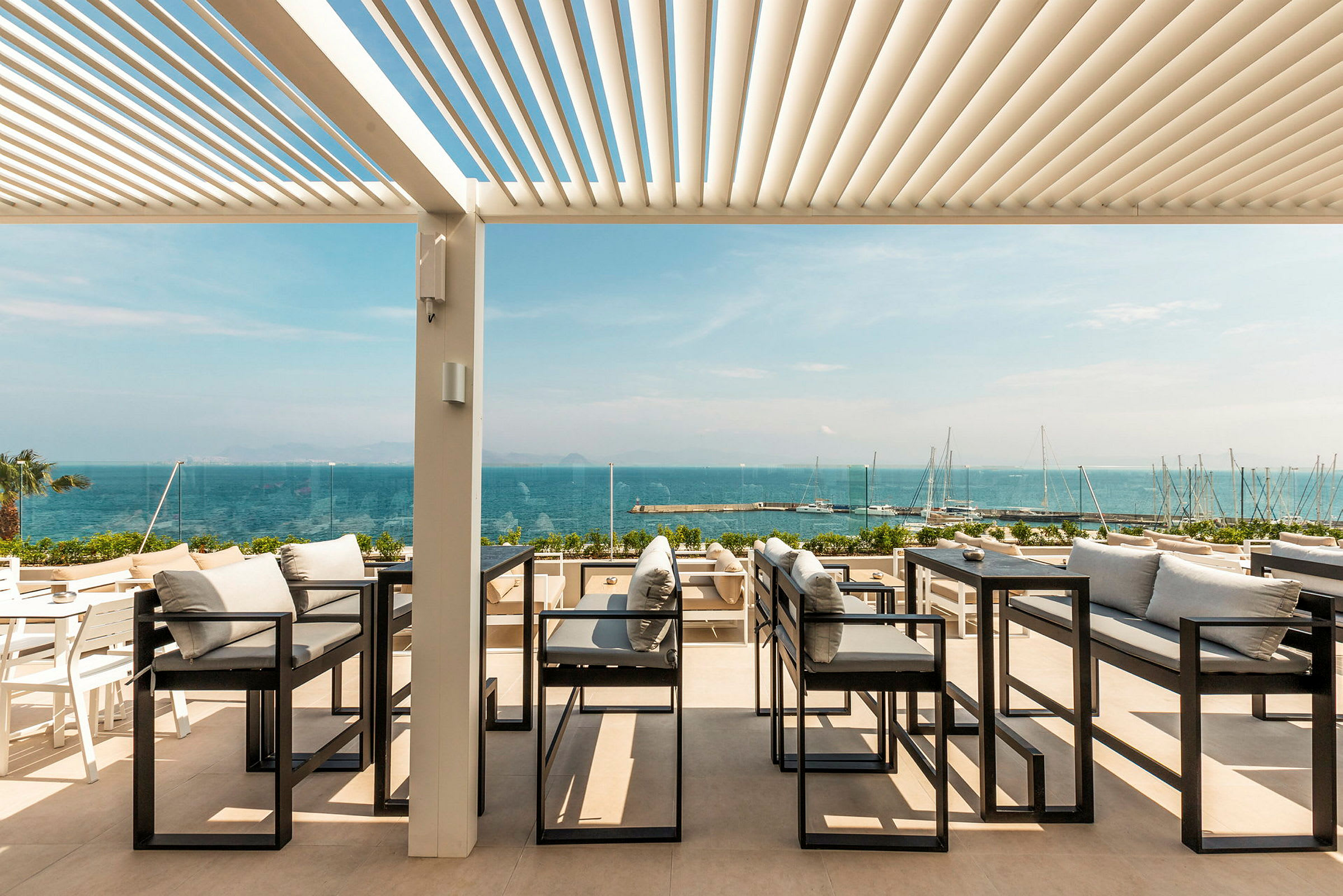 Uteservering med utsikt över havet, med soffor och bord under en pergola. (AI-genererad text)