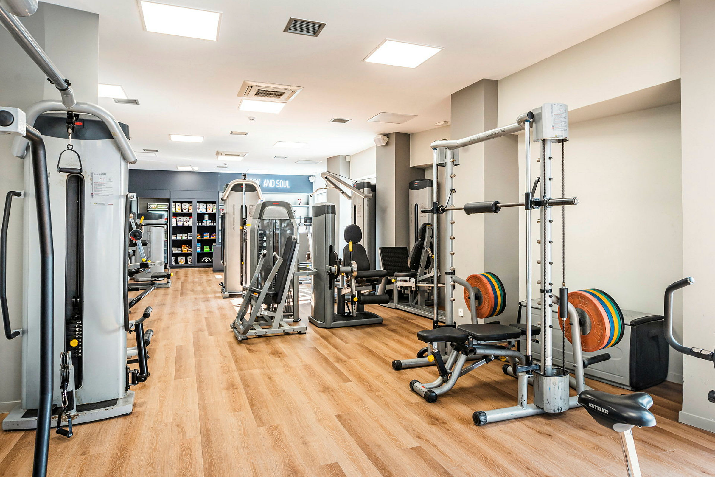 Ett gym med olika träningsmaskiner på ett golv av trälaminat. (AI-genererad text)