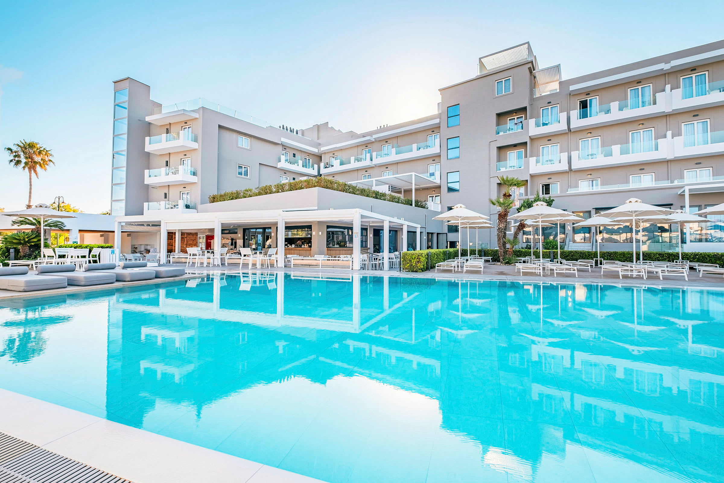 Ett hotell med en stor pool framför och sittplatser under parasoller. (AI-genererad text)