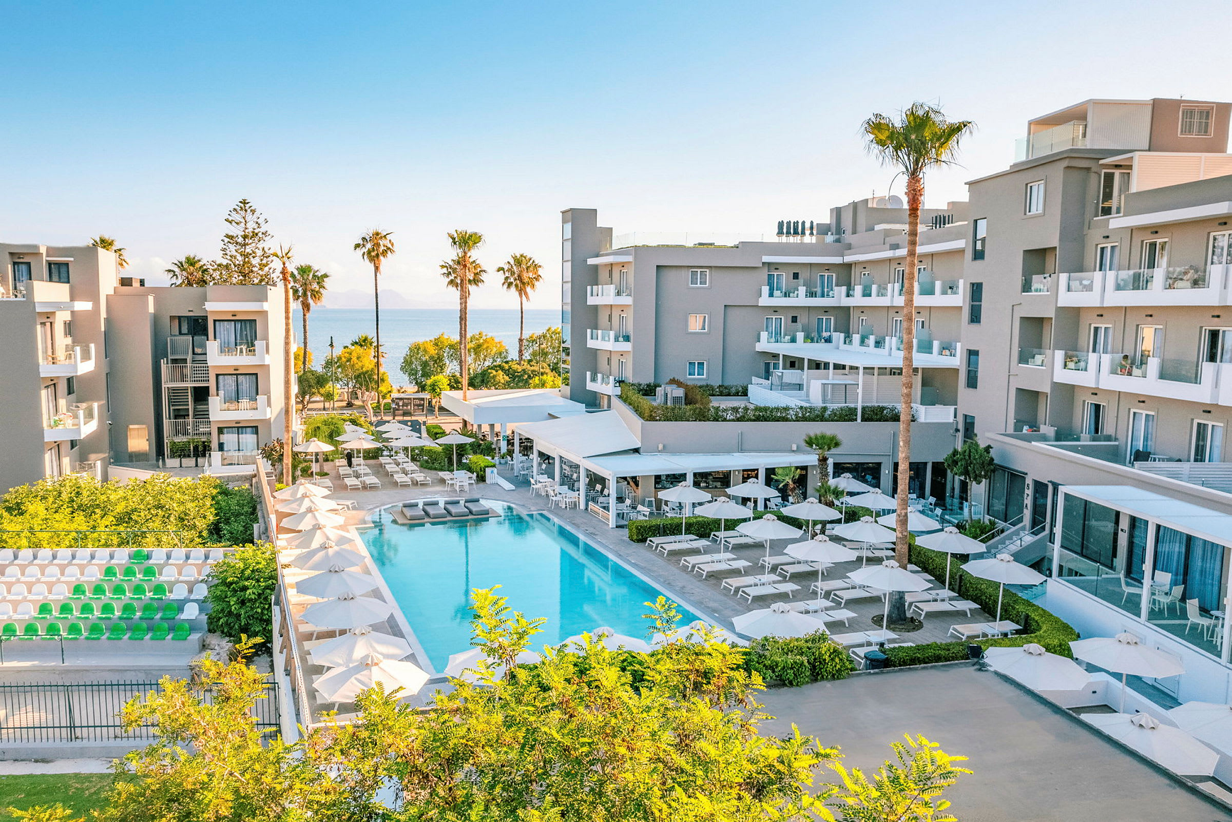 Ett modernt hotellkomplex med pool, solstolar och parasoller, omgiven av grönska och med utsikt över havet. (AI-genererad text)