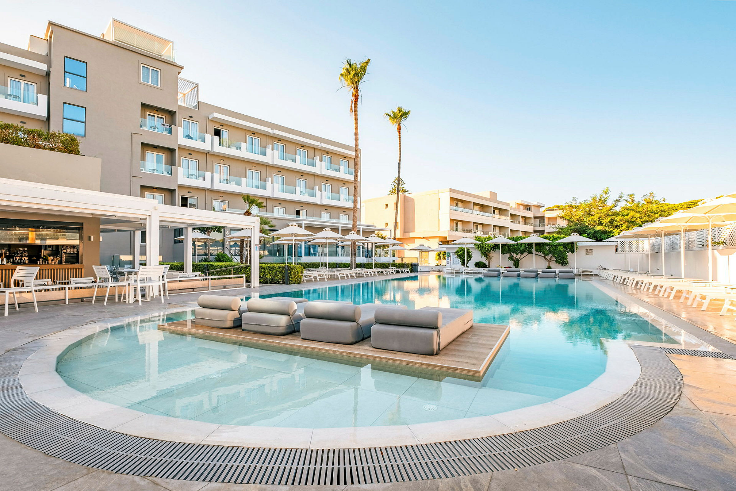 En hotellpool omgiven av solstolar och parasoller, med en byggnad i flera våningar i bakgrunden. (AI-genererad text)
