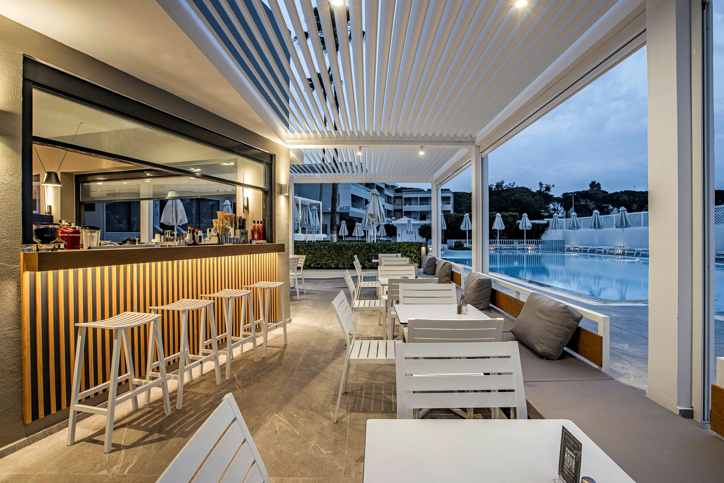 En utomhusbar och sittgrupp intill en pool med moderna vita möbler. (AI-genererad text)