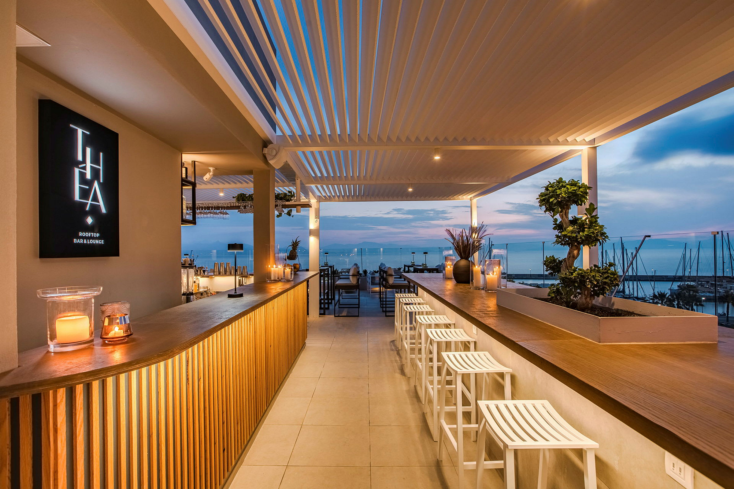 En modern takterrassbar med utsikt över havet i solnedgången. Baren är belyst och mysigt inredd. (AI-genererad text)