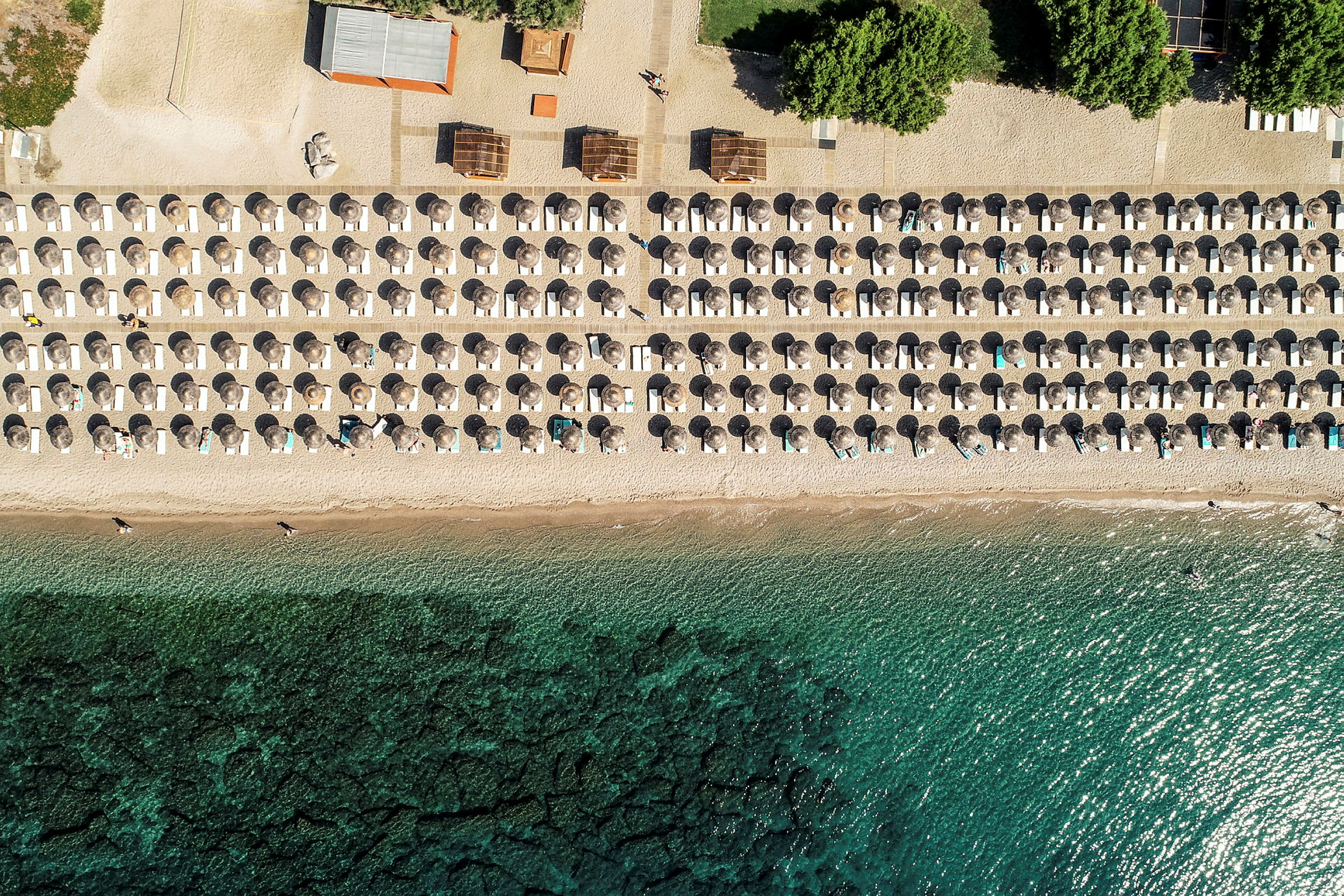 Flygbild av en strand med parasoller och solstolar i symmetriska rader vid stranden. (AI-genererad text)