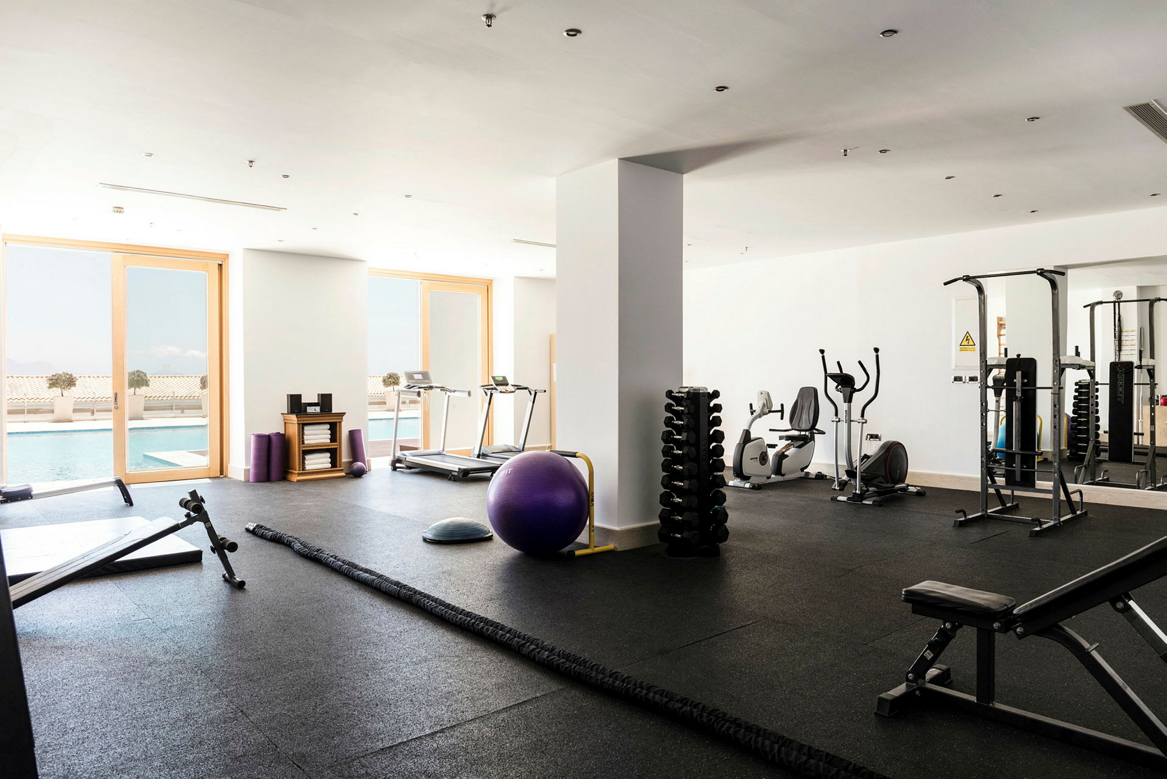 Bild på ett gym med träningsutrustning och utsikt mot en pool. (AI-genererad text)