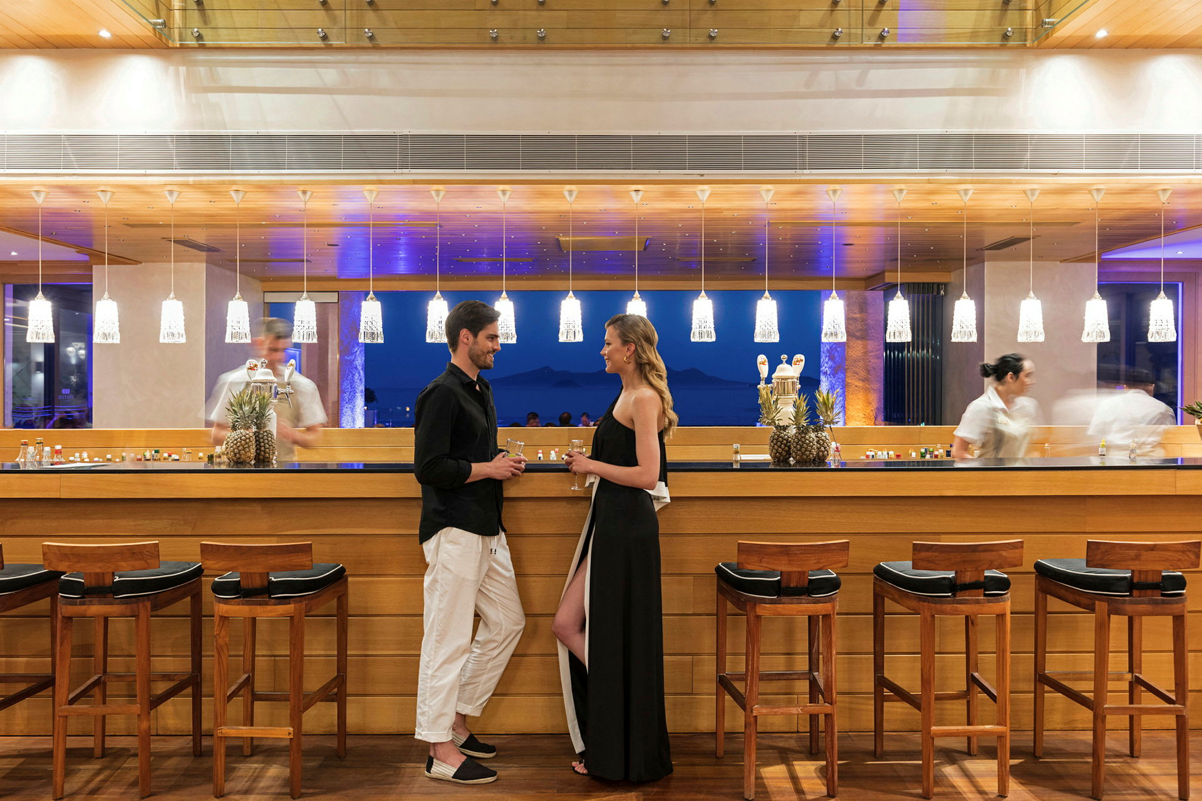 Personer står vid en elegant bar med träinredning och belysning. (AI-genererad text)
