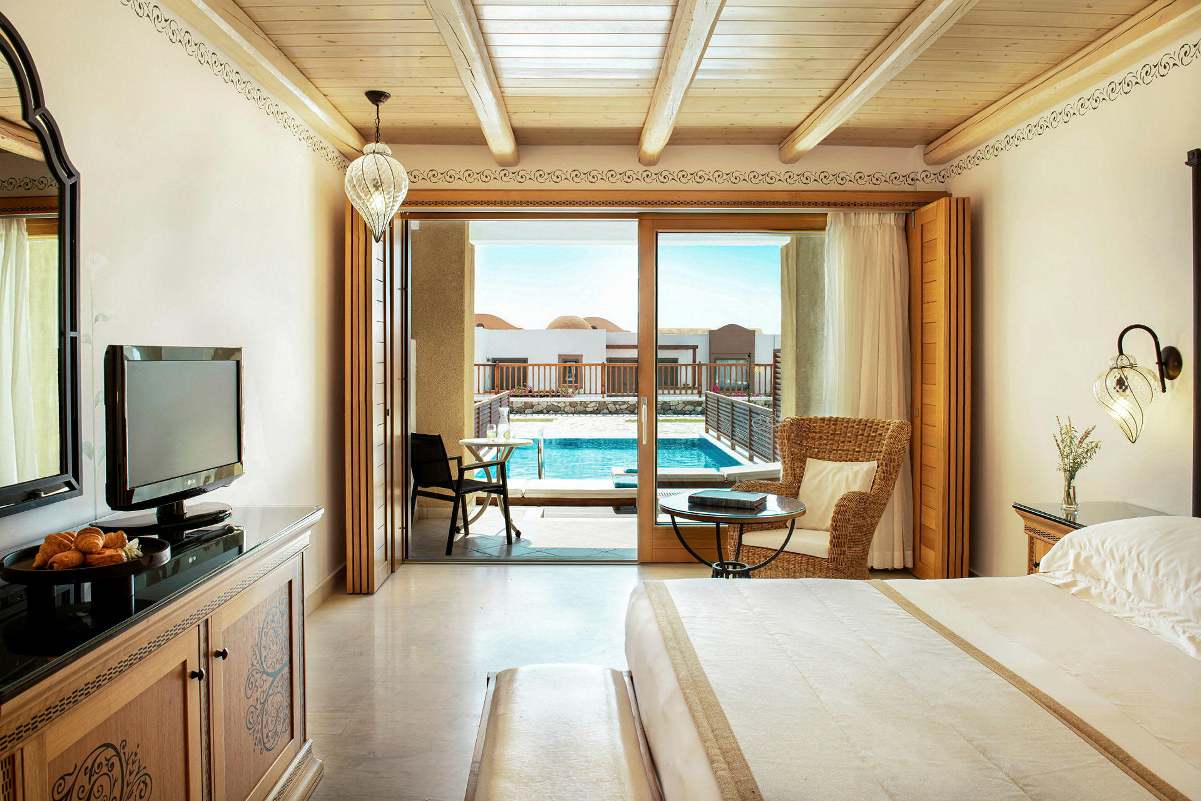 Hotellrum med trädetaljer inklusive en stor säng och en sittgrupp, samt en balkongdörr som leder till en pool. (AI-genererad text)