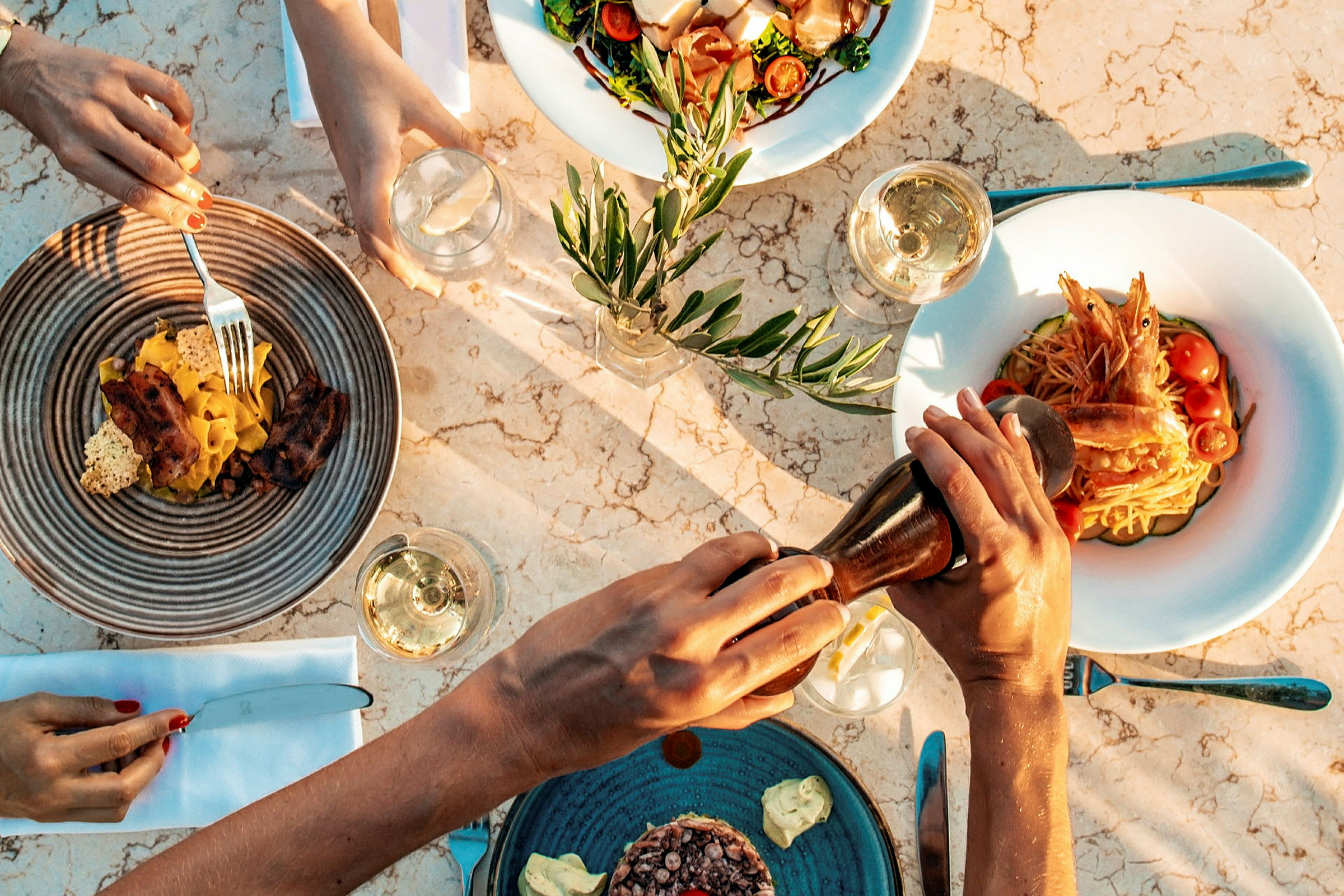Fyra tallrikar med olika maträtter och glas med dryck på en marmorbord. (AI-genererad text)