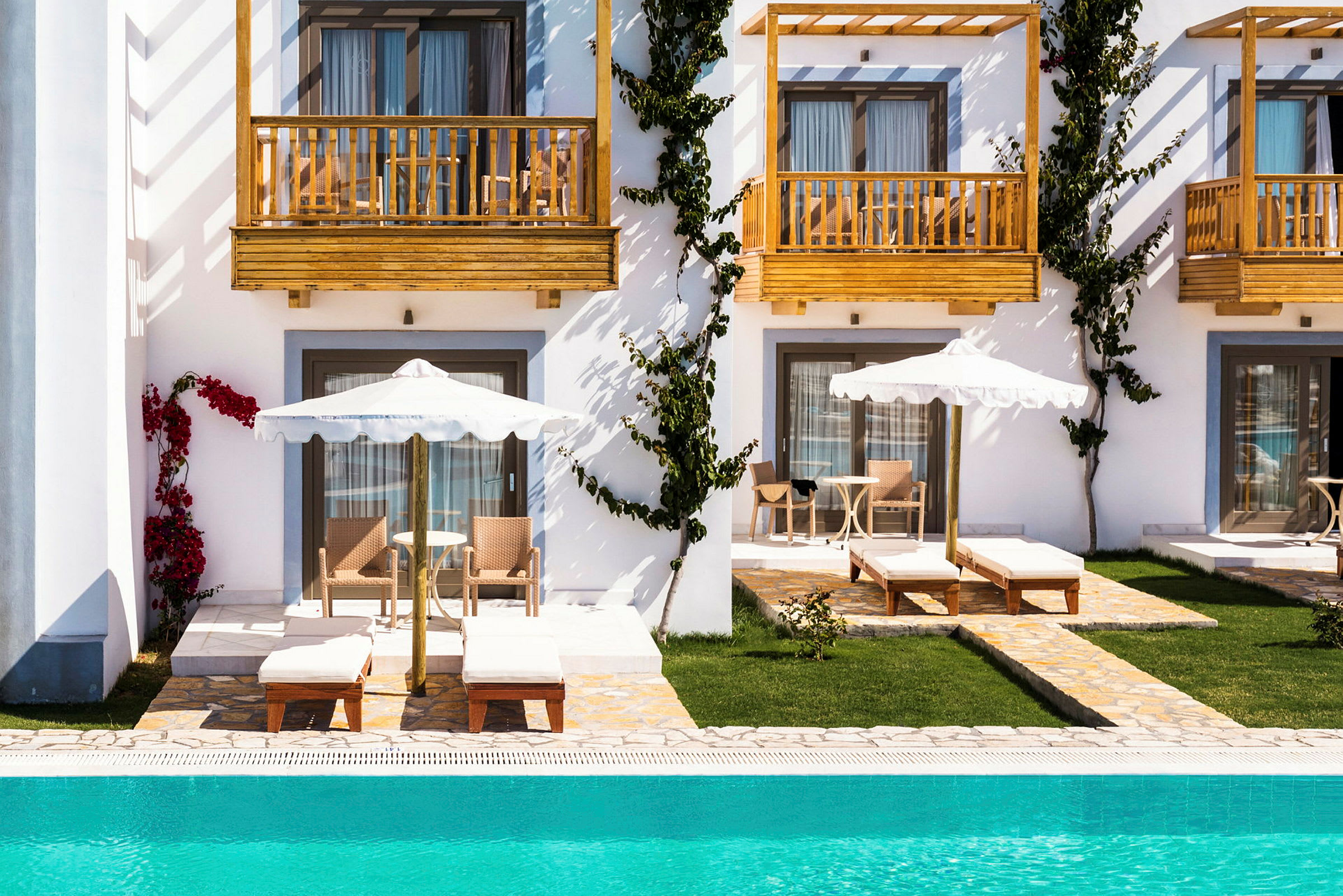 Vit byggnad med träbalkonger och solstolar vid pool. (AI-genererad text)